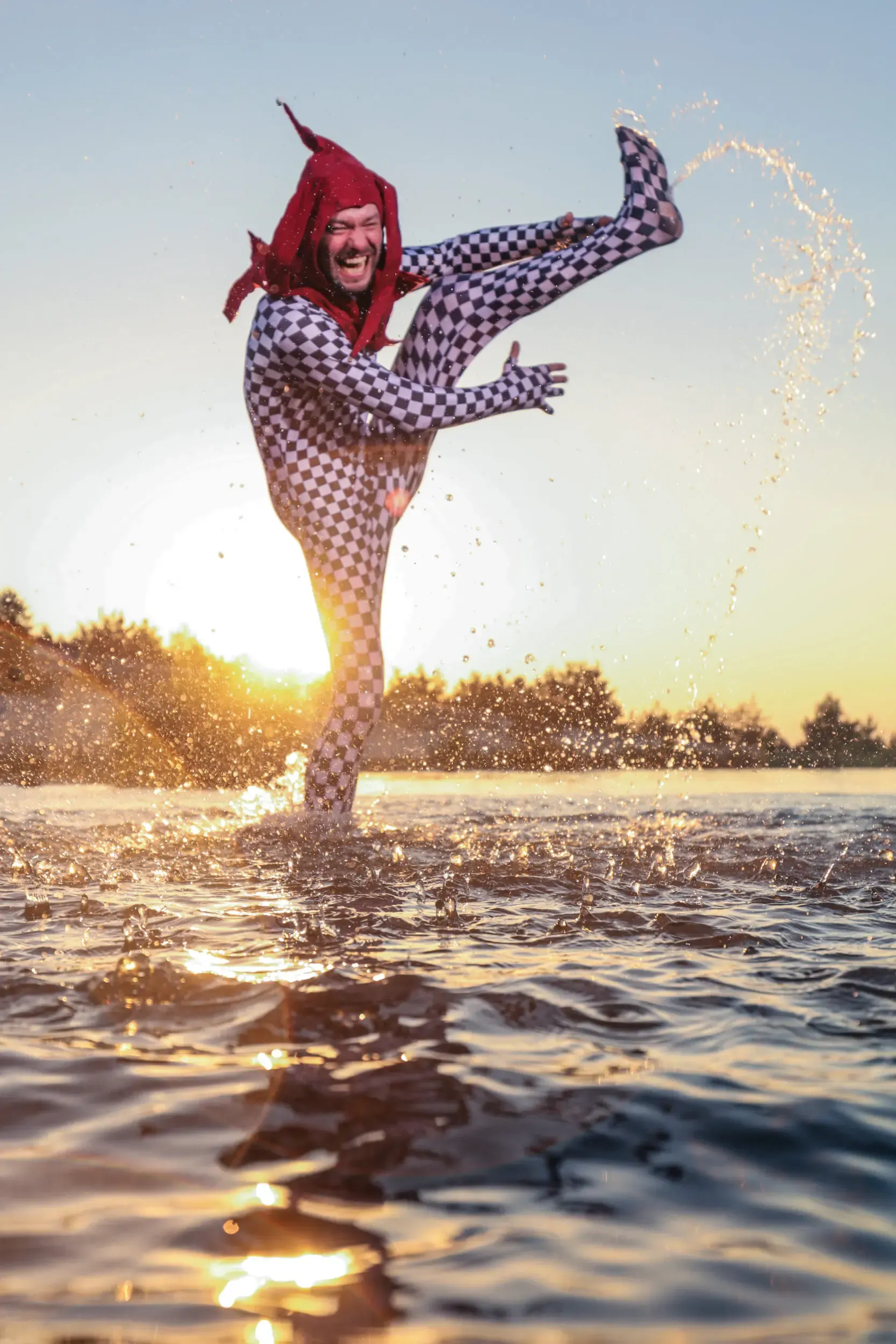 Schauspieler springt lachend aus dem Wasser im Gegenlicht des Sonnenuntergangs
