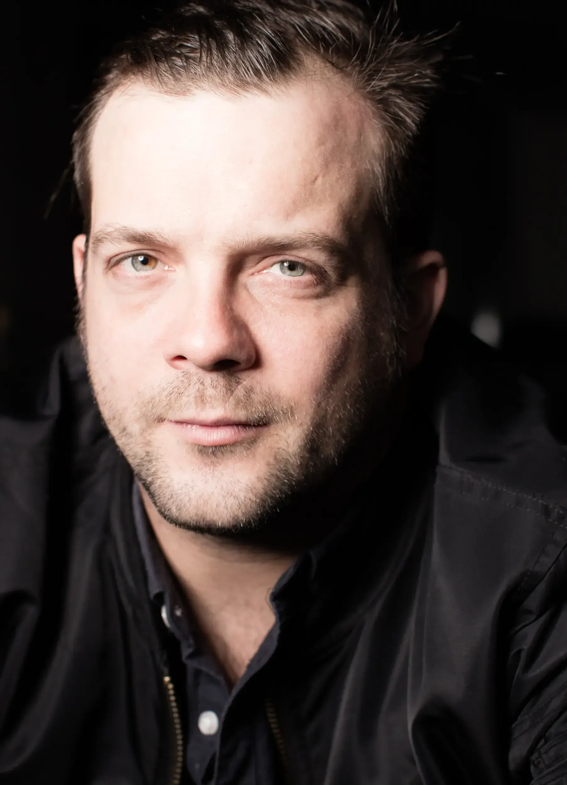 Close-up portrait of André Willmund in a black jacket, lit dramatically against a dark background.