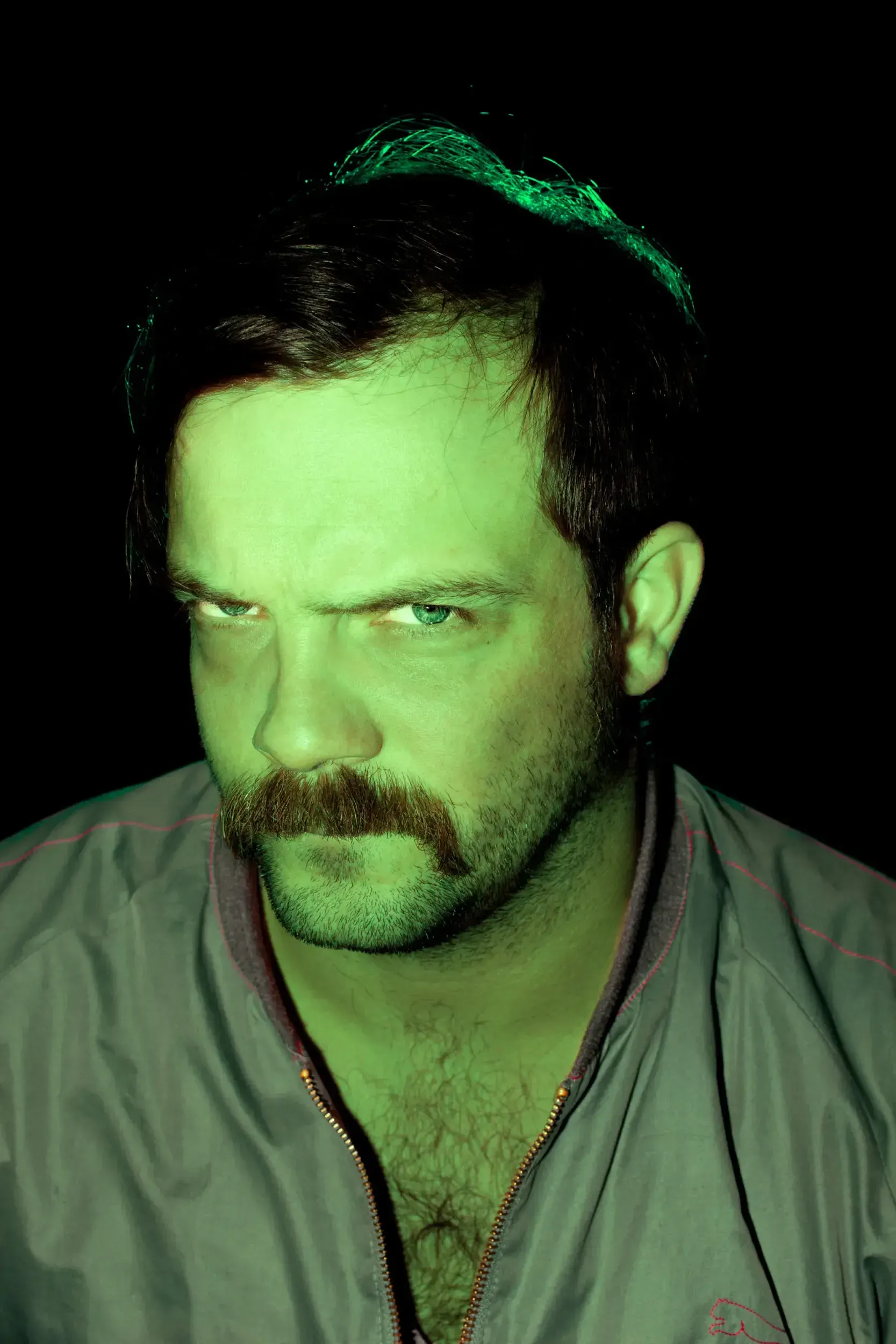 Portrait of André Willmund with a stern expression, his face lit entirely in green light against a black background.
