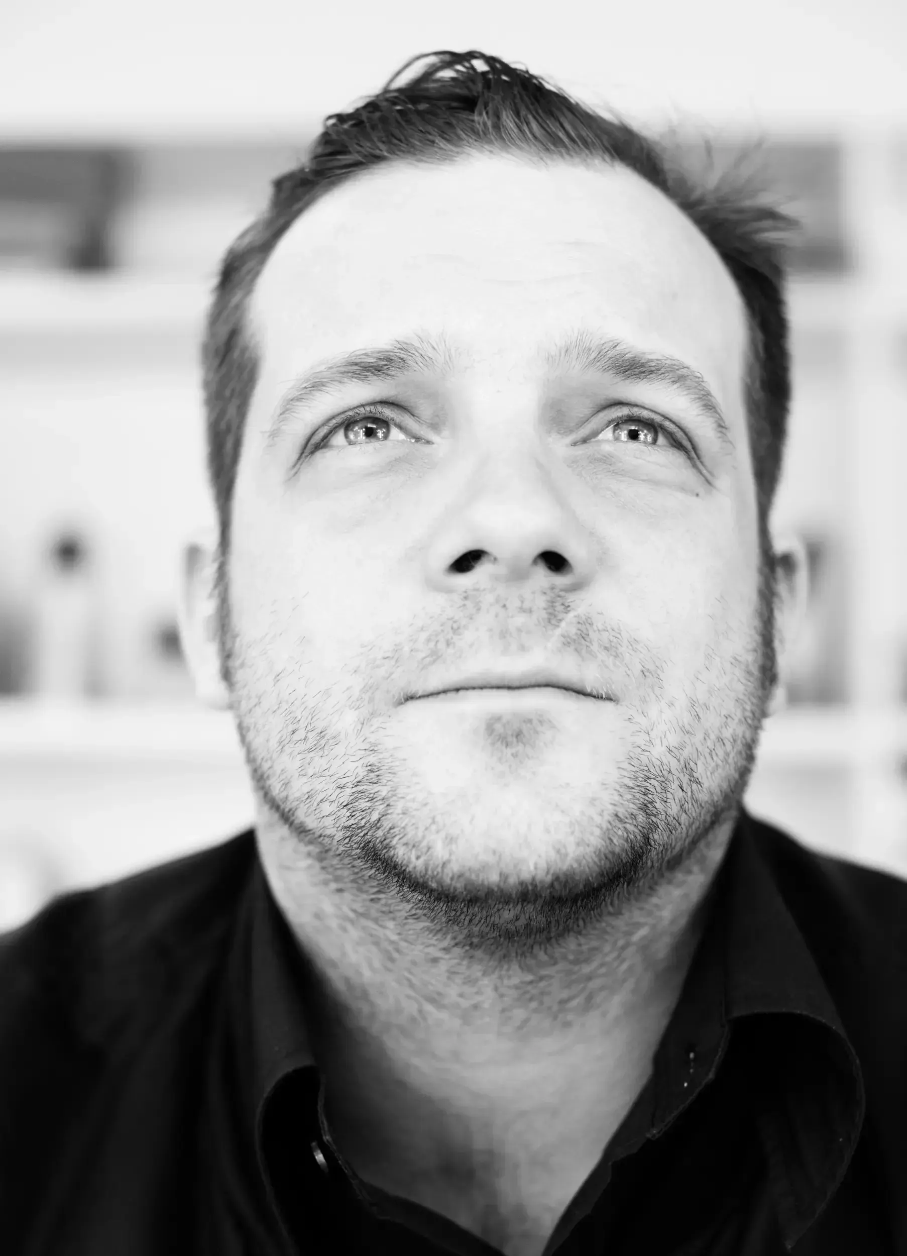 Black-and-white close-up portrait of André Willmund looking straight up, bookshelves blurred in the background.