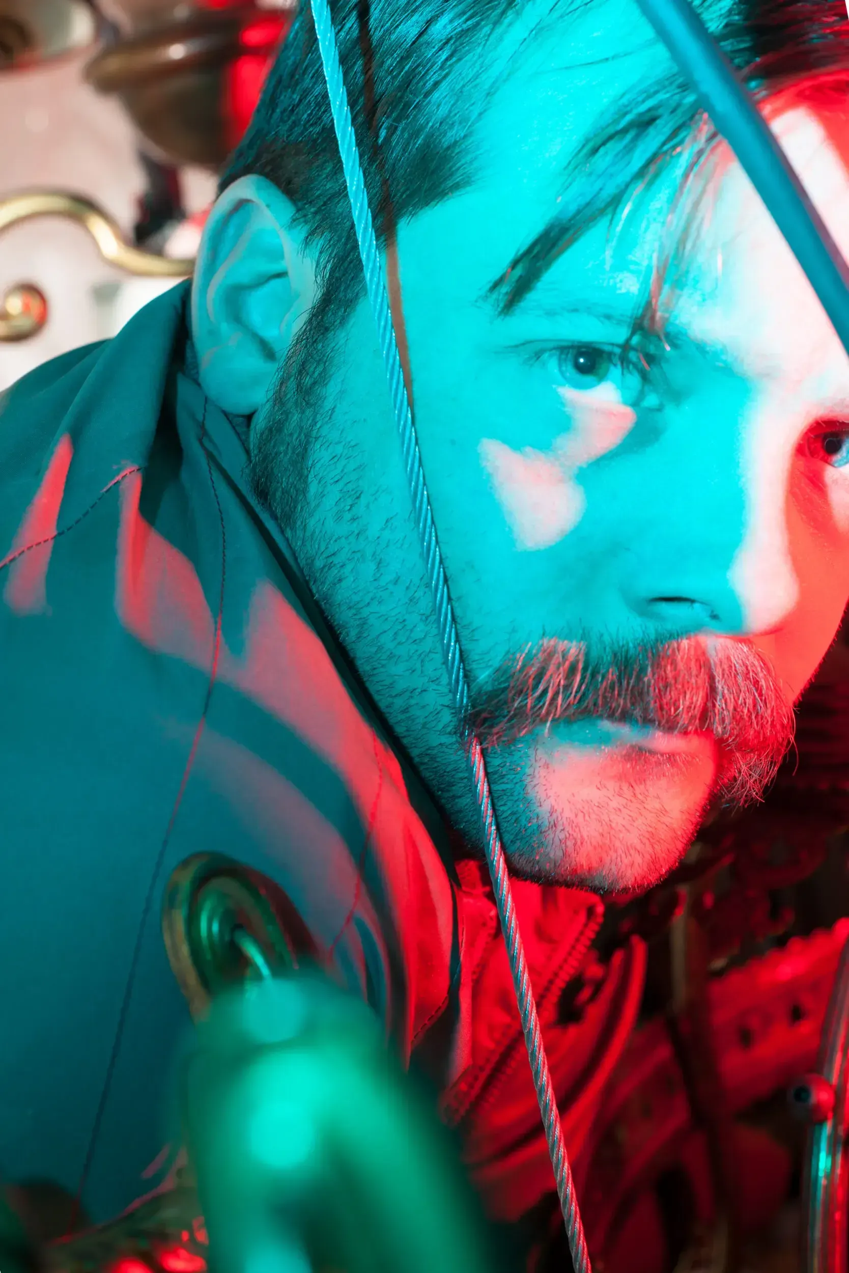 Close-up portrait of André Willmund lit in dramatic red and teal gel light, looking past a cable in the foreground.