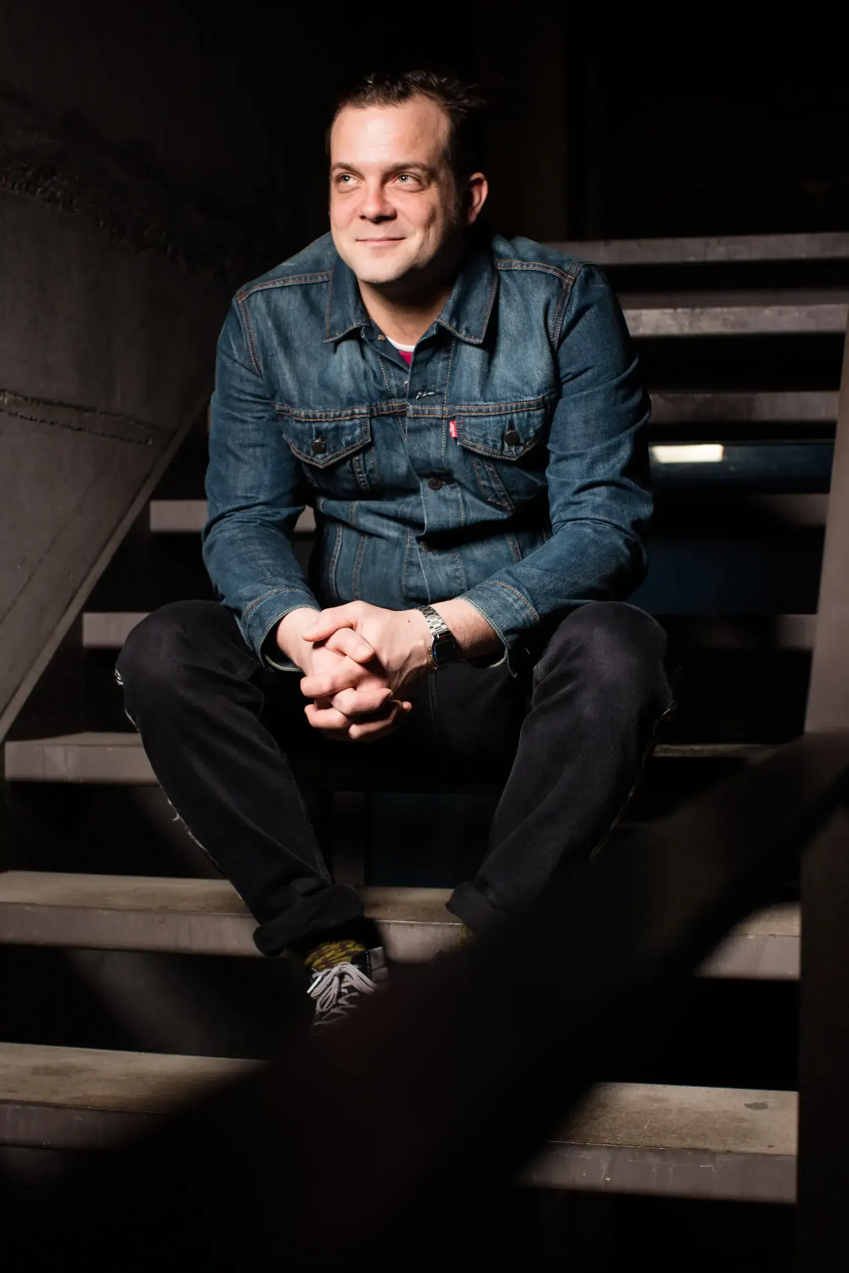 André Willmund sitting on a staircase with hands clasped, smiling and looking upward.