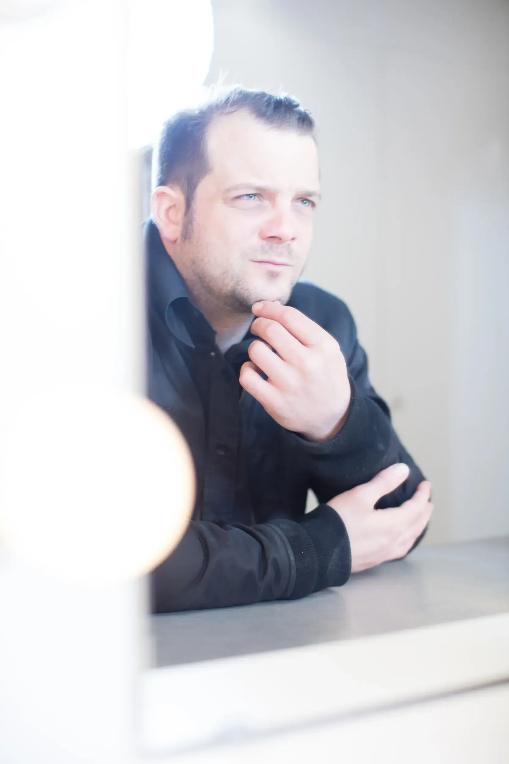 Portrait of André Willmund resting his chin on his hand in soft window light.