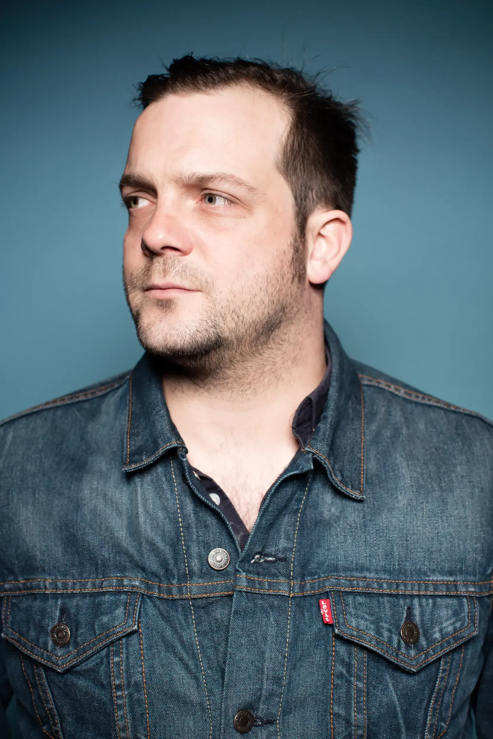 Studio portrait of André Willmund in a denim jacket against a blue background, glancing to the side.