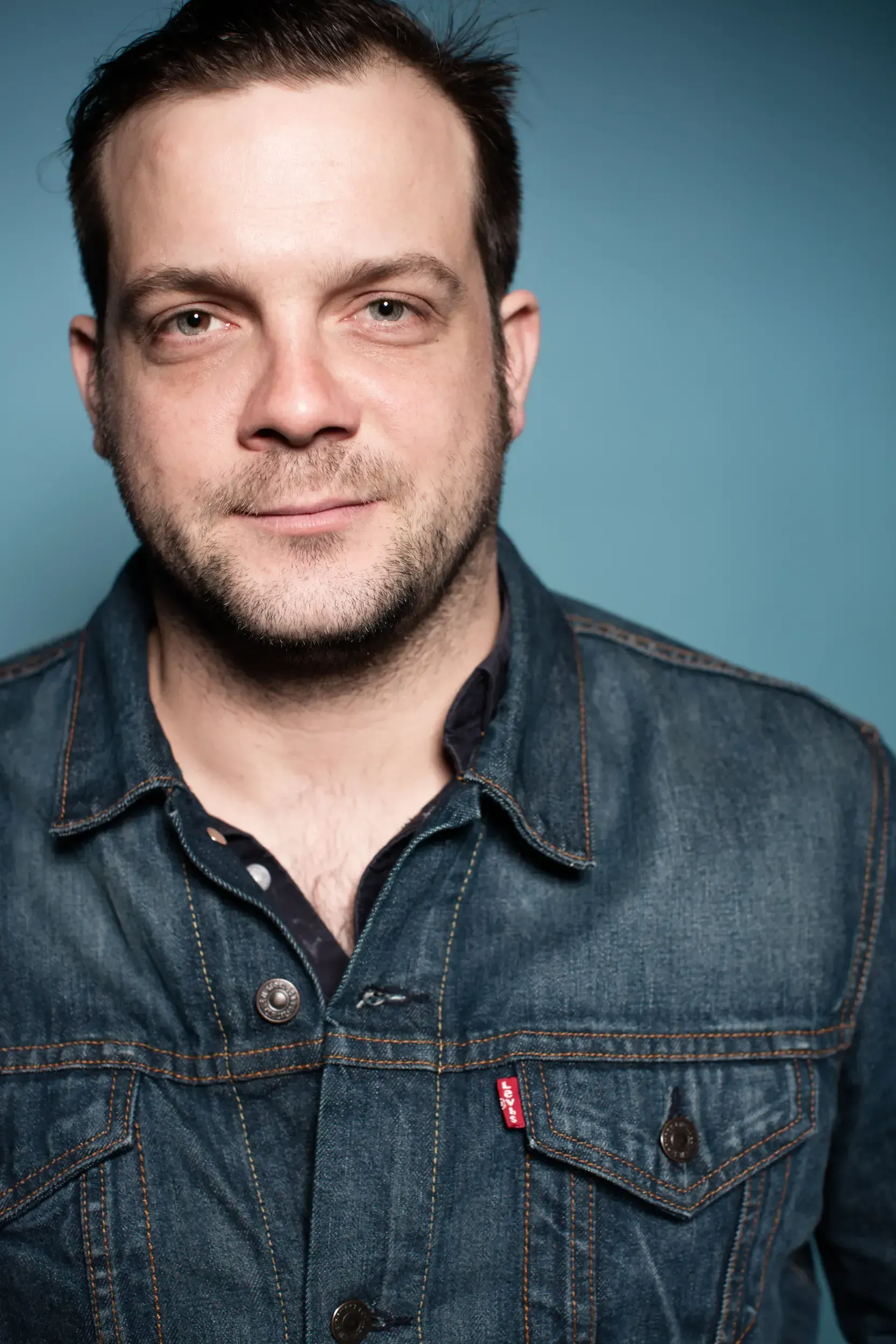 Studio portrait of André Willmund in a denim jacket against a blue background, facing the camera.