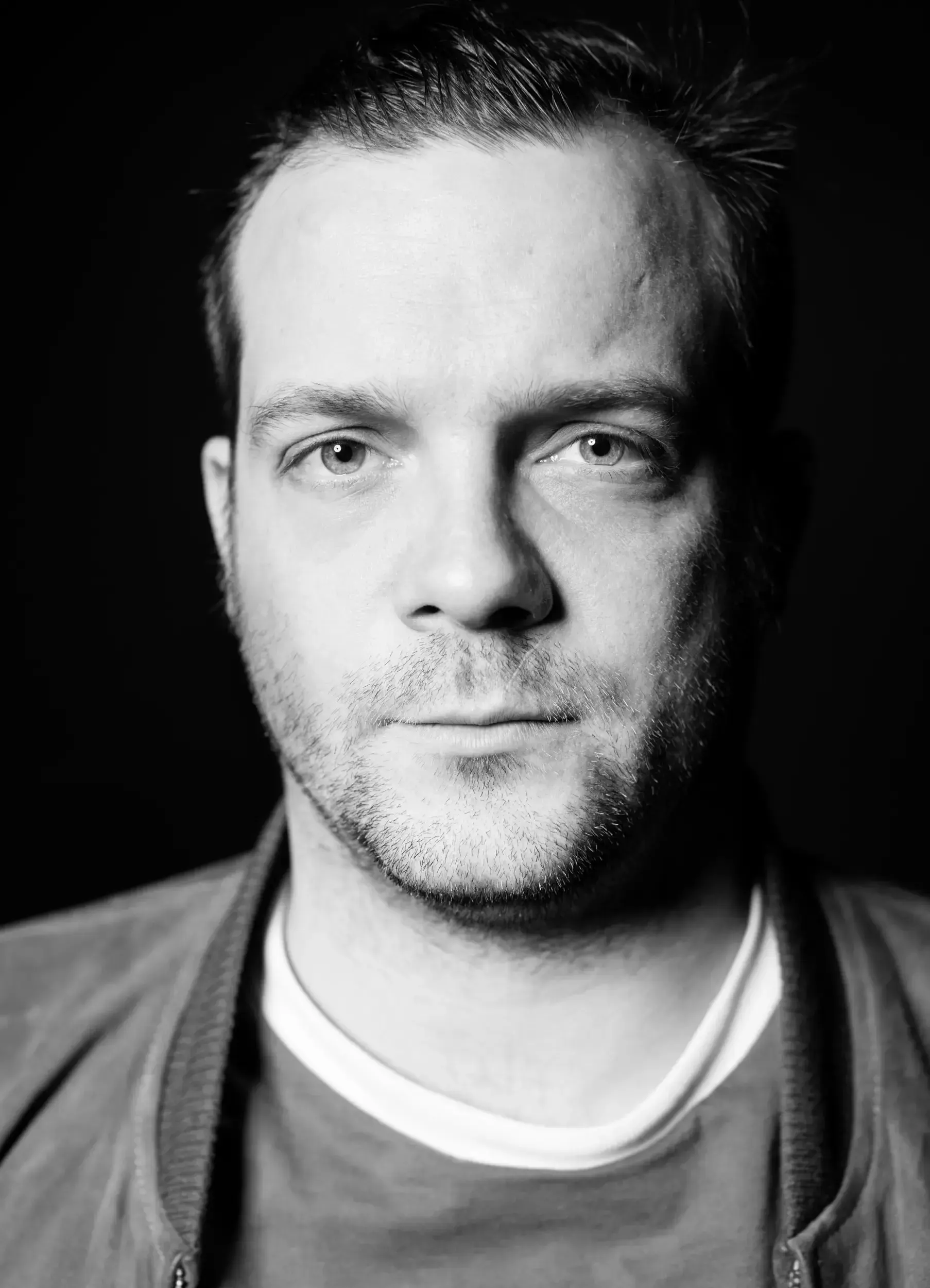 Black-and-white studio portrait of André Willmund wearing a jacket against a black background.