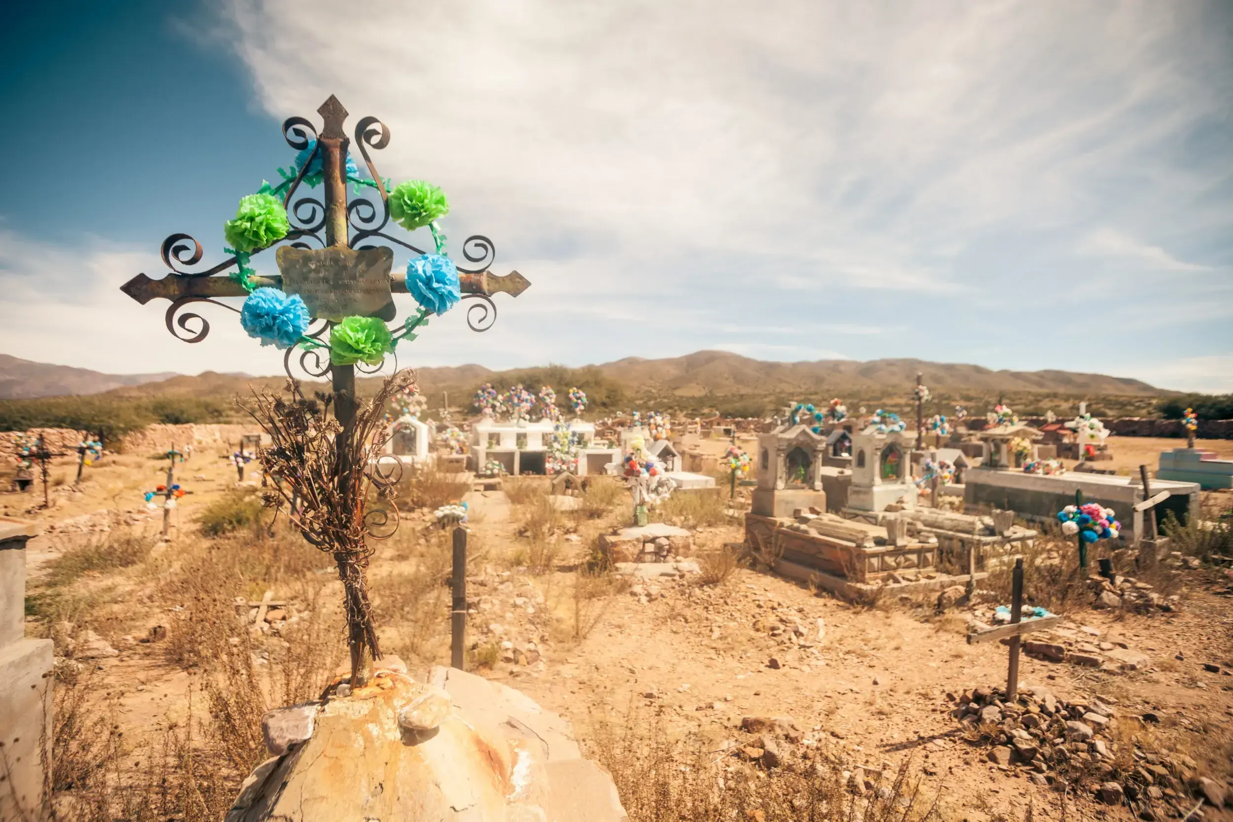Ornate iron cross decorated with paper flowers in a rural Argentine cemetery.