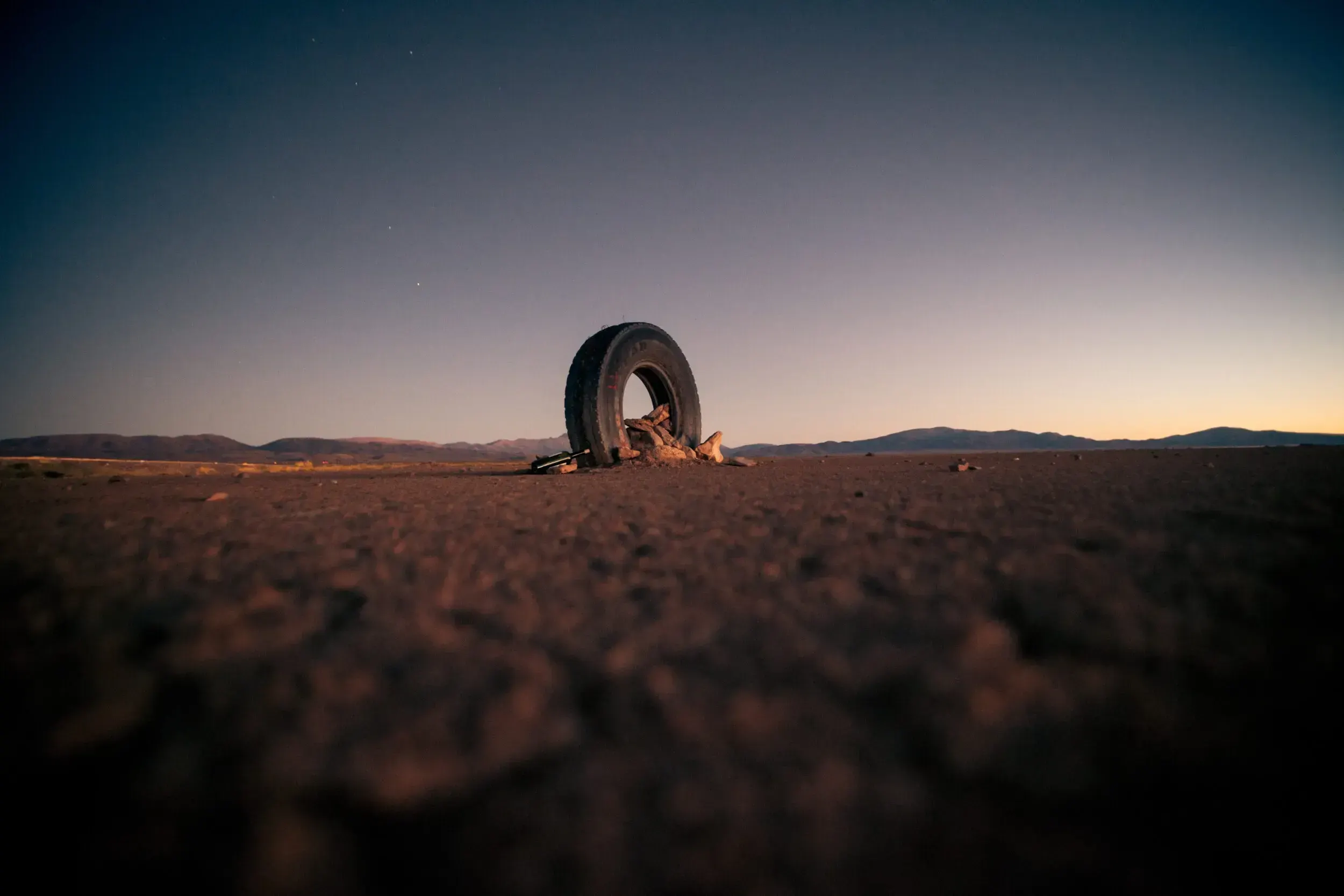 Weathered tire standing upright in the desert of Argentina at dusk, with stars appearing in the sky.