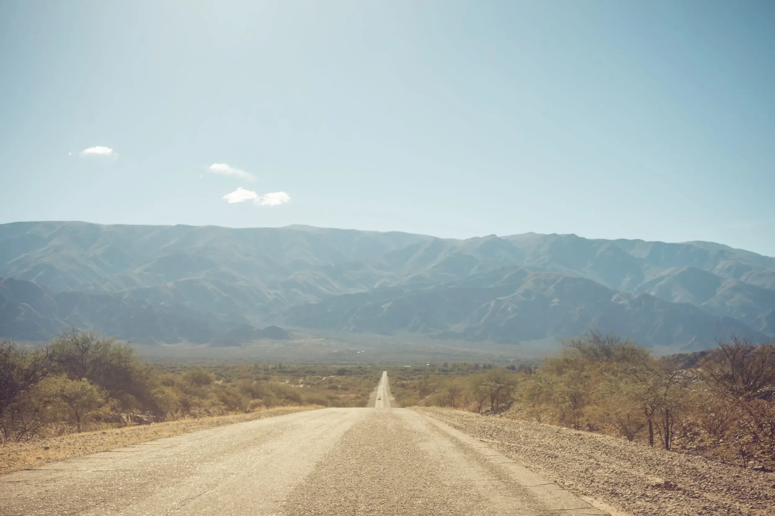 Straight dirt road leading toward hazy mountains in the Argentine countryside.