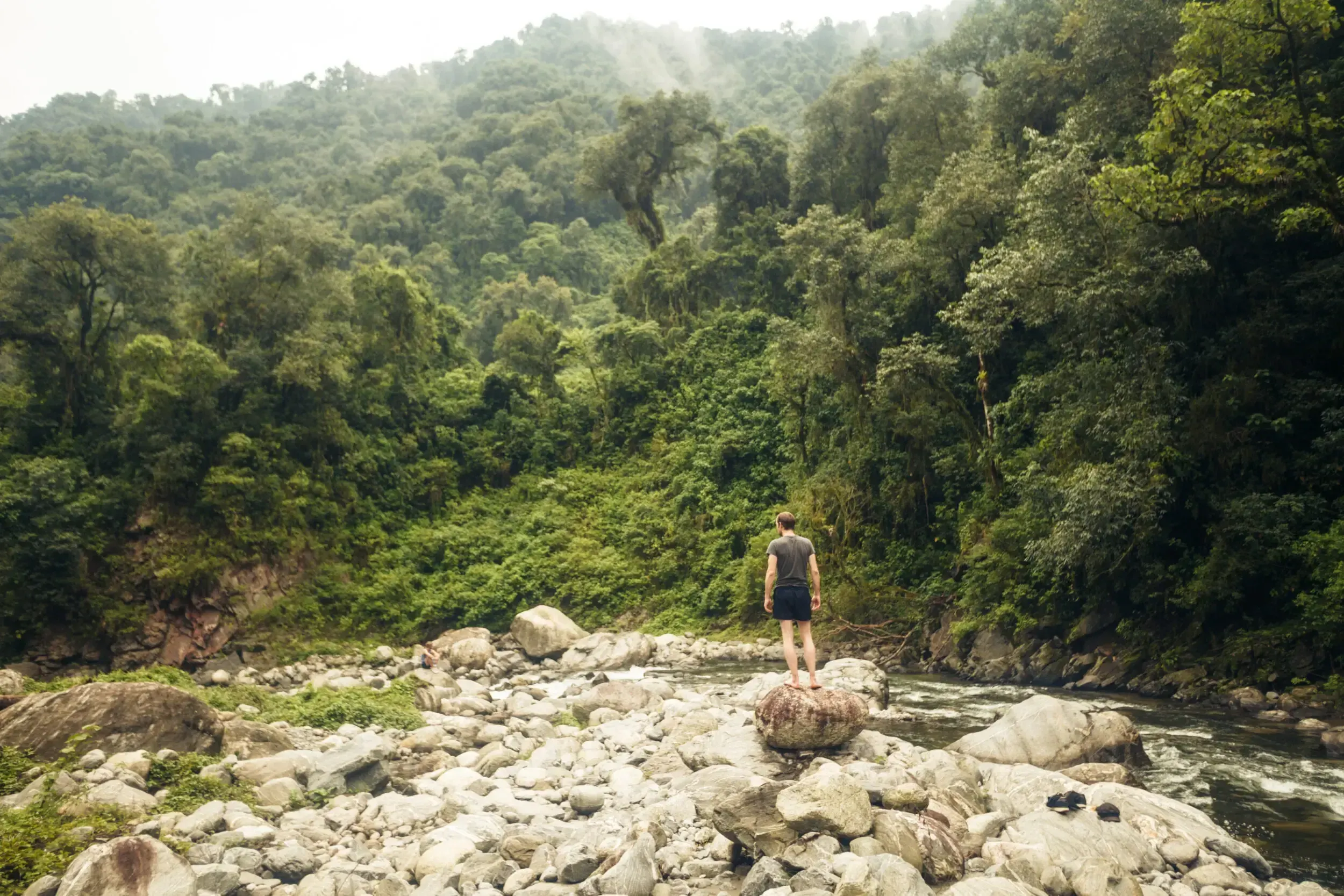 Hiker standing on a boulder overlooking a rocky river surrounded by dense jungle in Argentina.