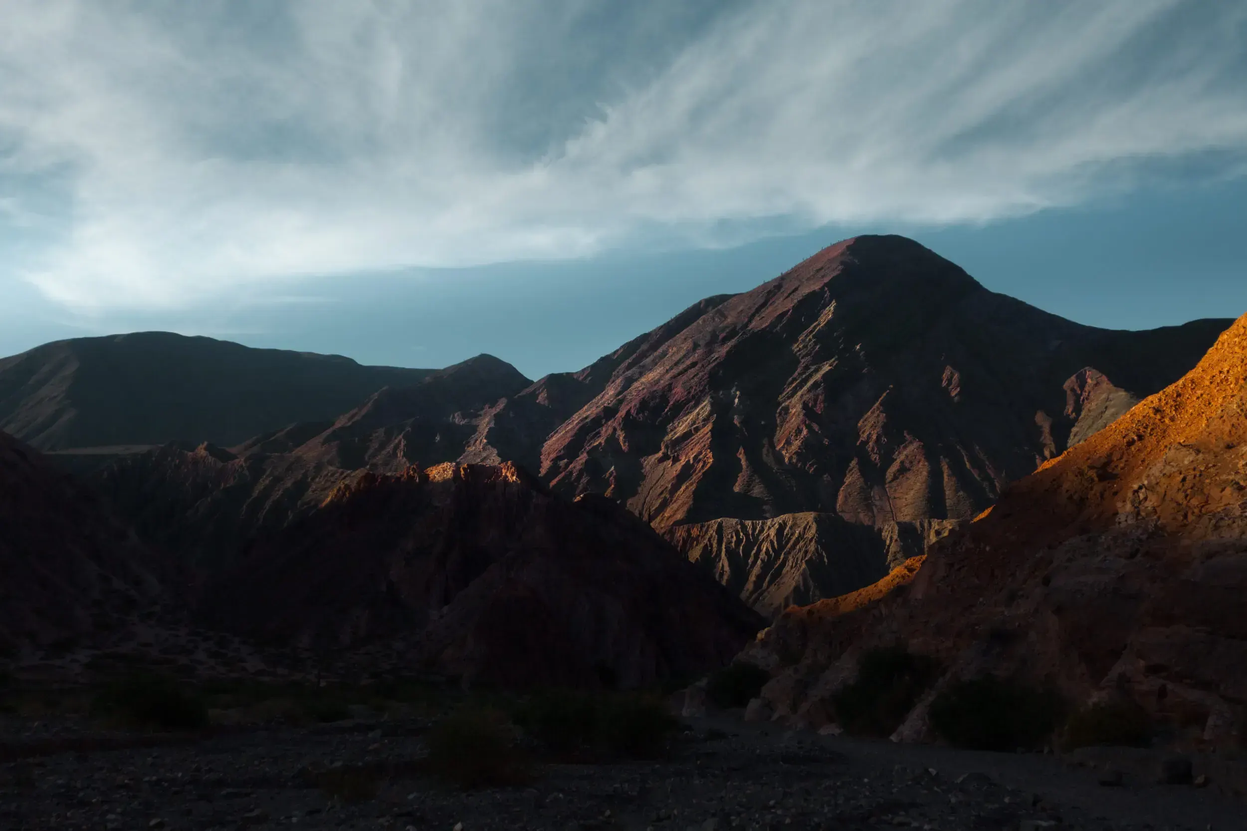 Rugged mountain range in Argentina lit by warm evening light beneath a cloudy sky.
