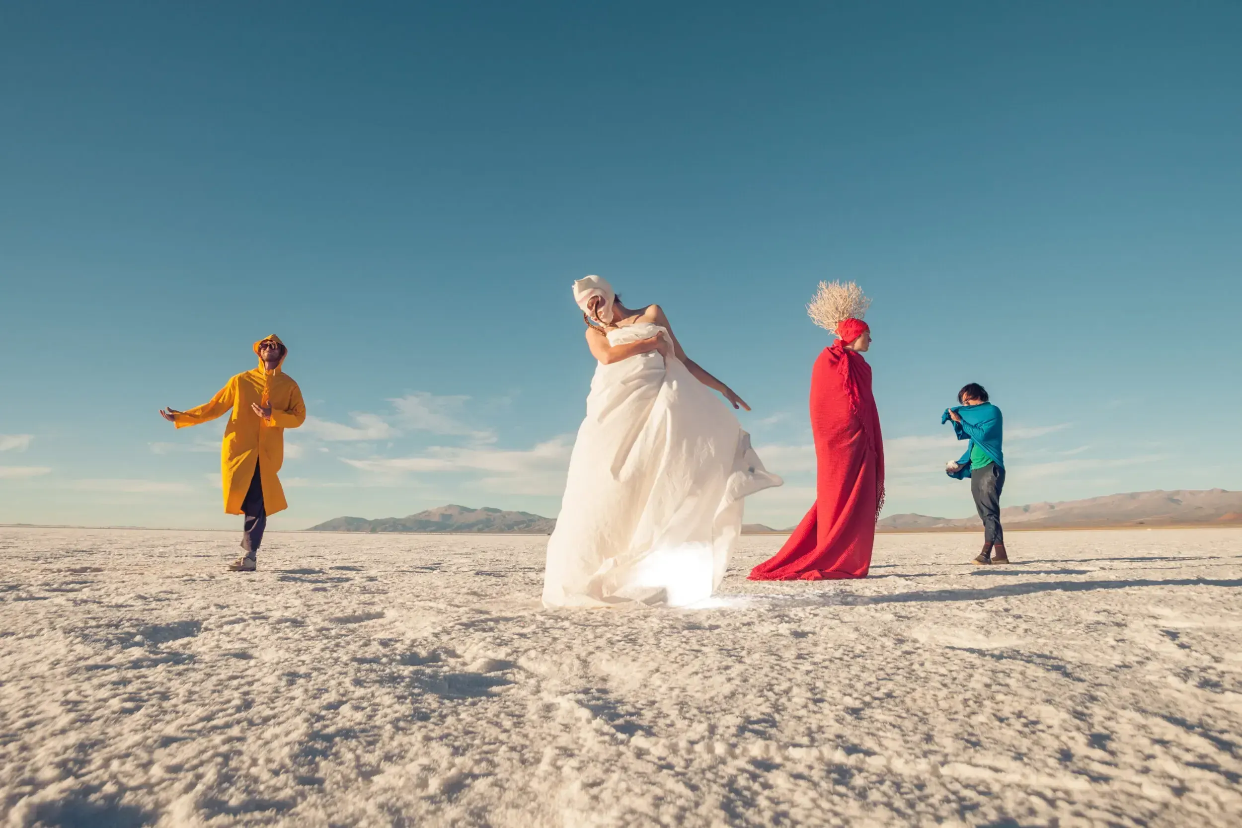 Four costumed performers in colorful robes posing on the white salt flats of Argentina.