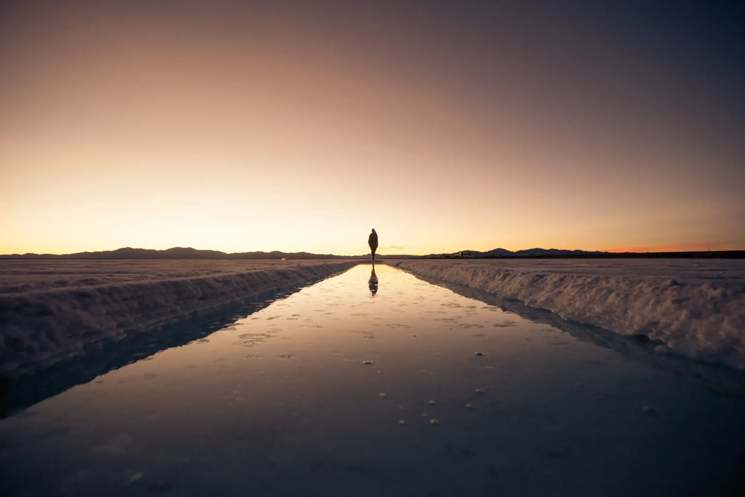 Silhouette of a person walking along a flooded salt flat reflecting the sunset in Argentina.