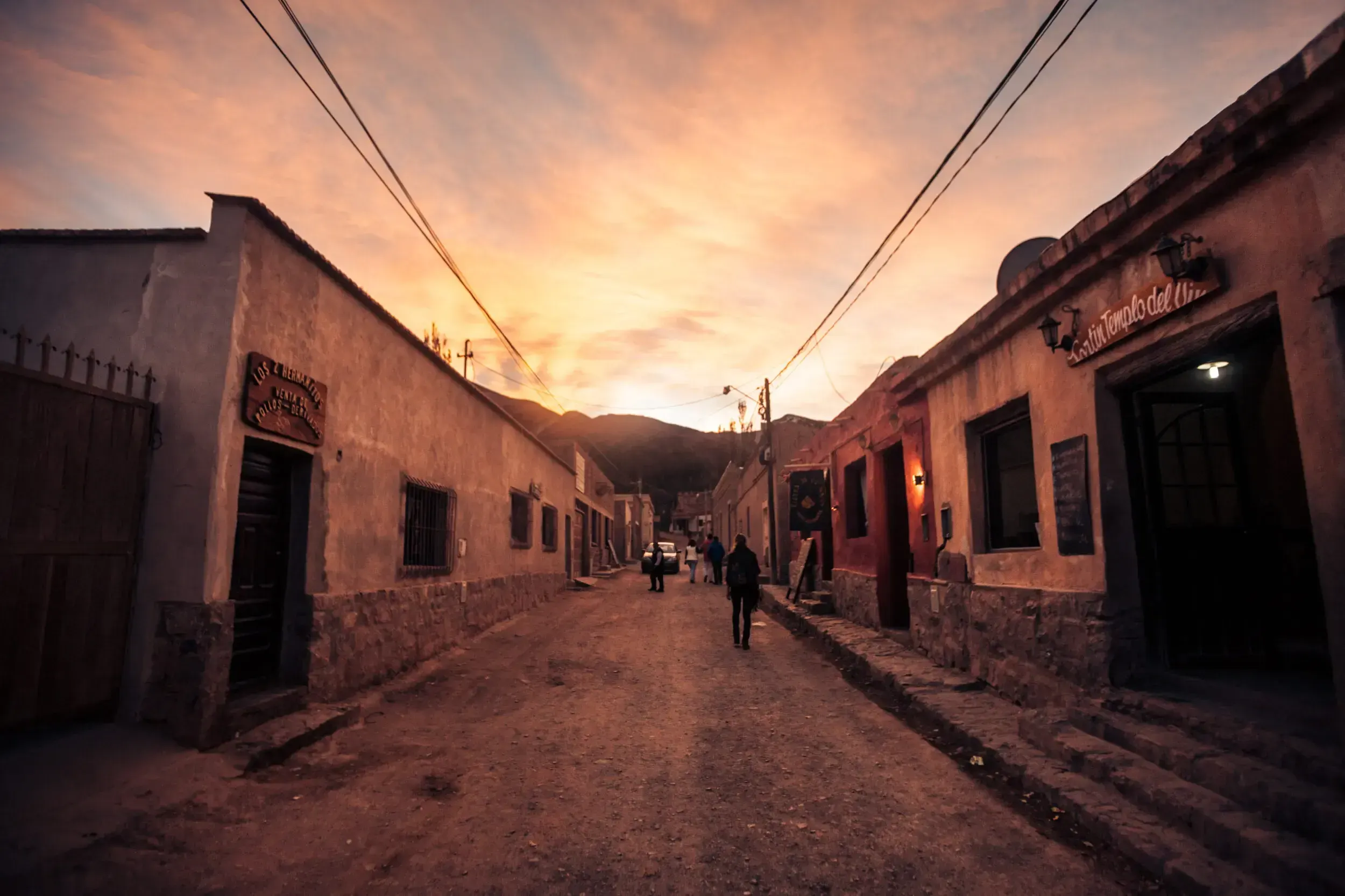 Narrow adobe street in a small Argentine village glowing under a colourful sunset sky.