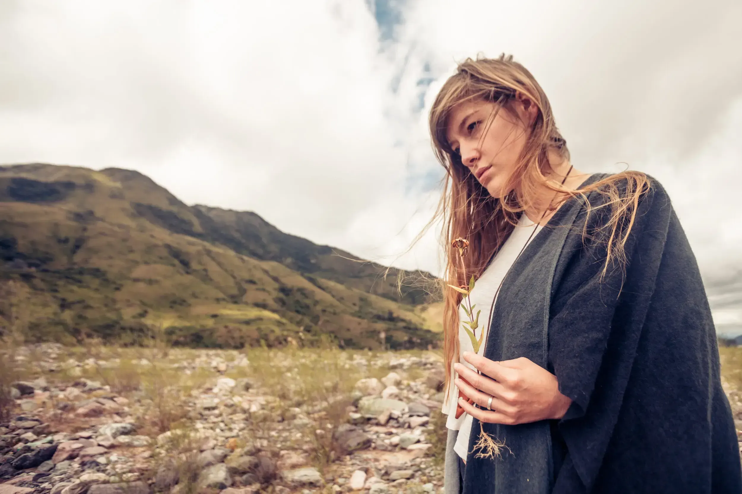 Woman wrapped in a shawl holding a wildflower, standing before mountains in Argentina.