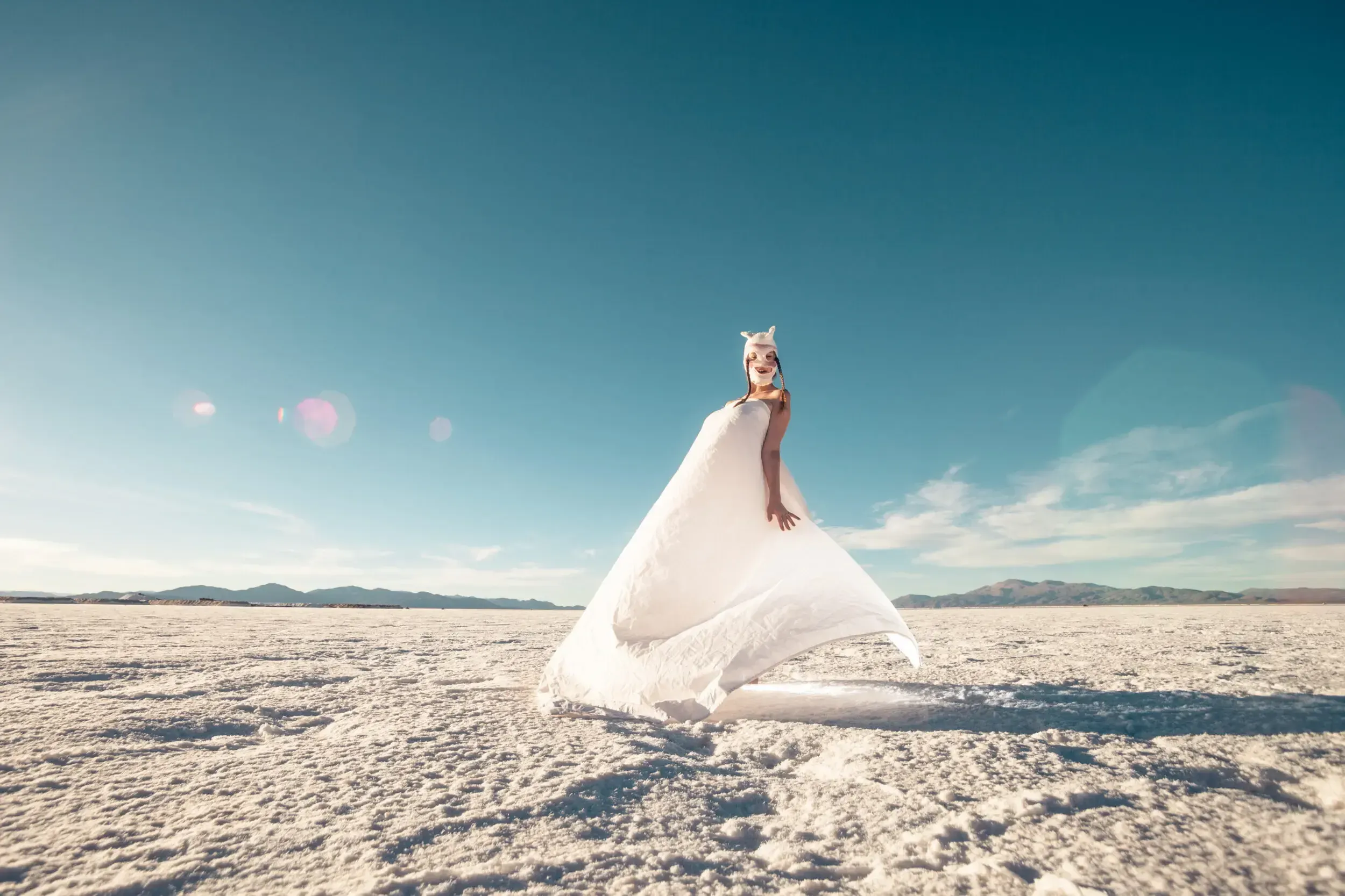 Woman in a flowing white dress and an animal-ear headpiece standing on the salt flats of Argentina.