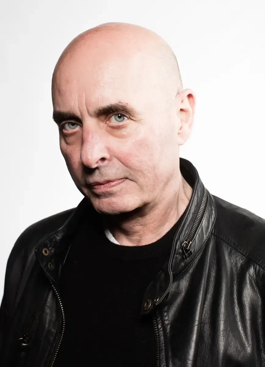 Studio portrait of a bald man in a black leather jacket against a white background.