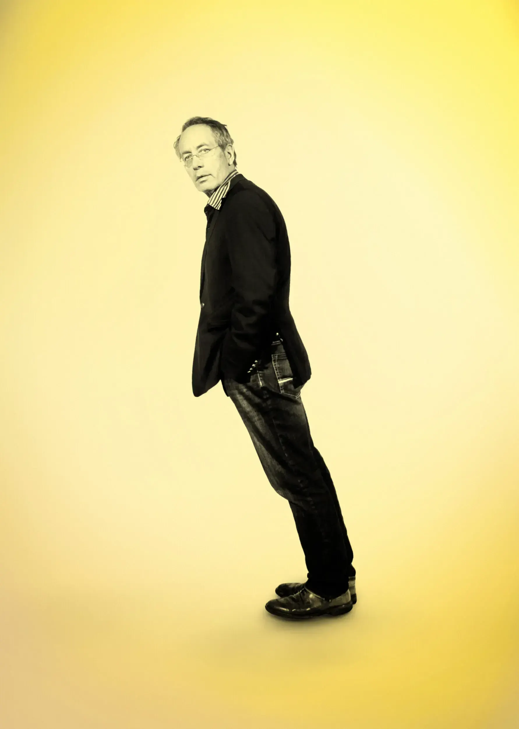Theatre actor recreating a Howard Jones album pose, leaning forward against a yellow background.