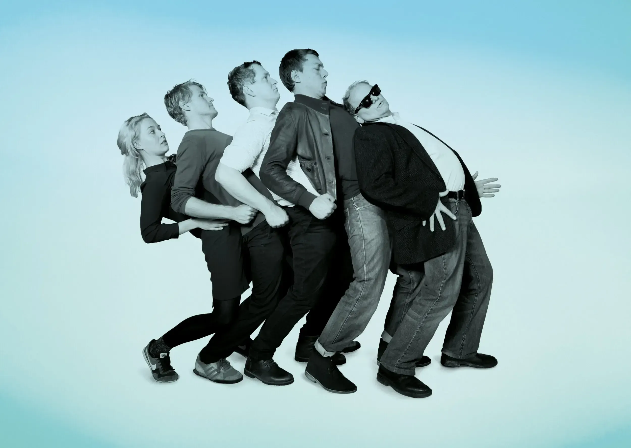 Theatre ensemble recreating the Madness 'One Step Beyond' leaning line pose against a blue background.