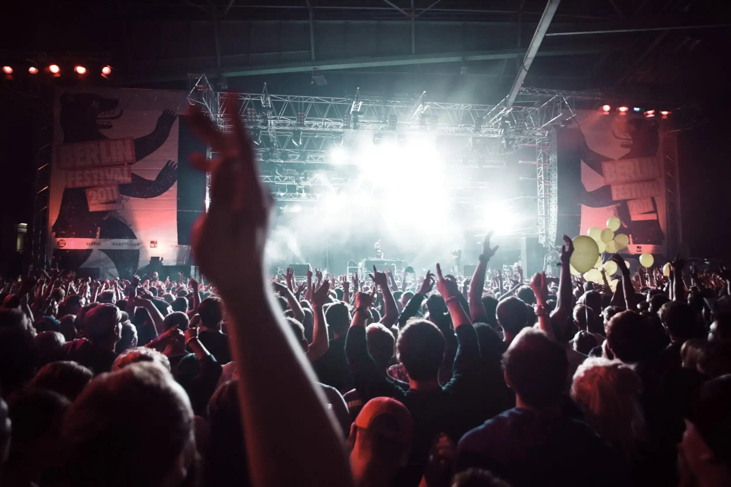 Crowd raising their hands in front of a brightly lit stage at Berlin Festival, with bear-logo banners on either side.