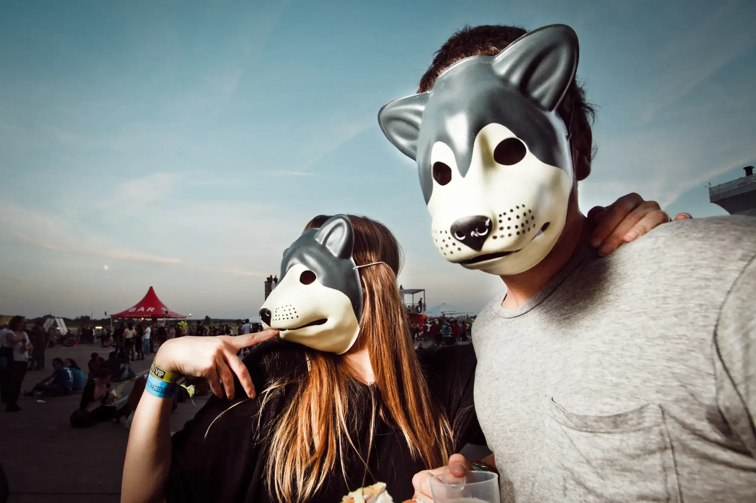 Couple wearing husky dog masks posing together at a festival at dusk.