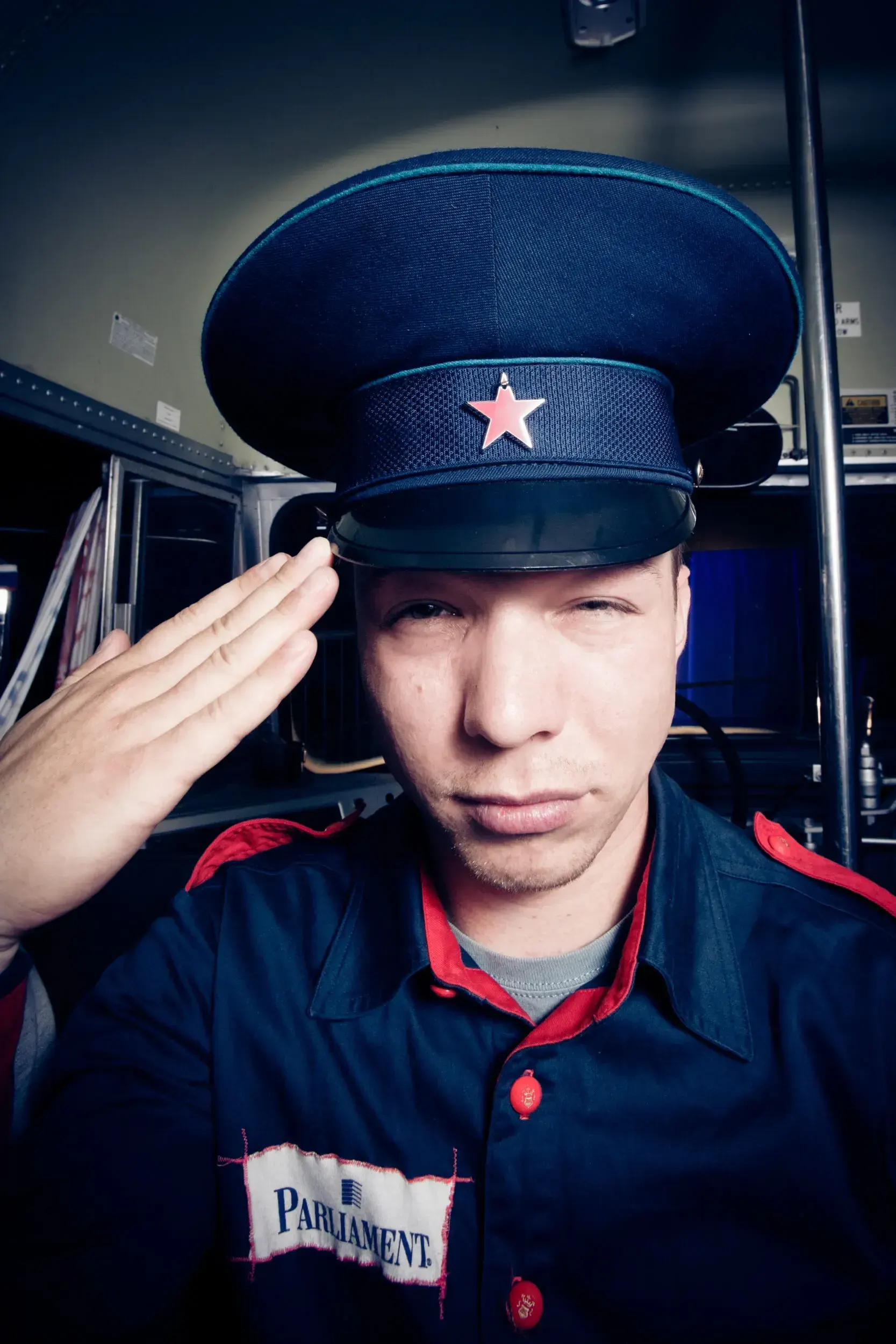 Man in a Soviet-style military cap with a red star saluting, wearing a Parliament-branded jacket backstage.