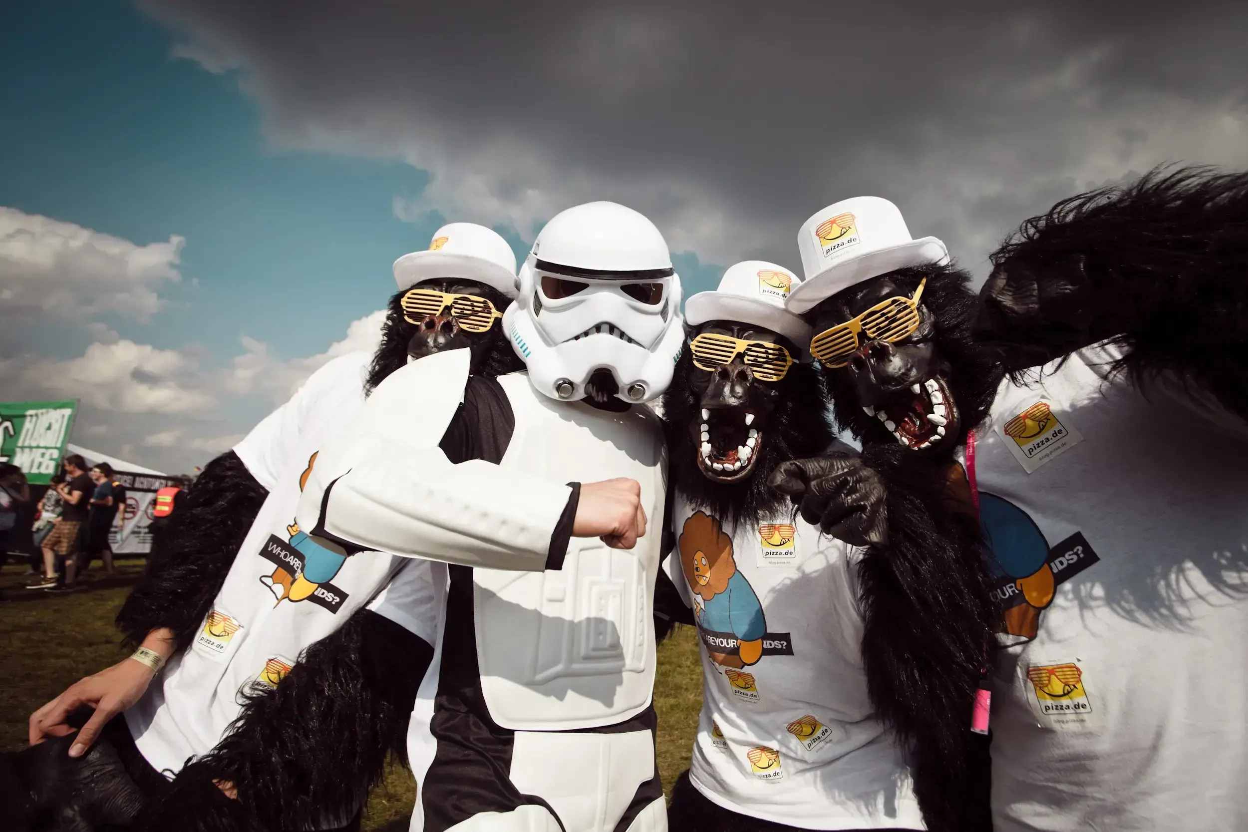 Festival-goers in a stormtrooper costume and gorilla masks wearing branded pizza.de top hats and t-shirts.