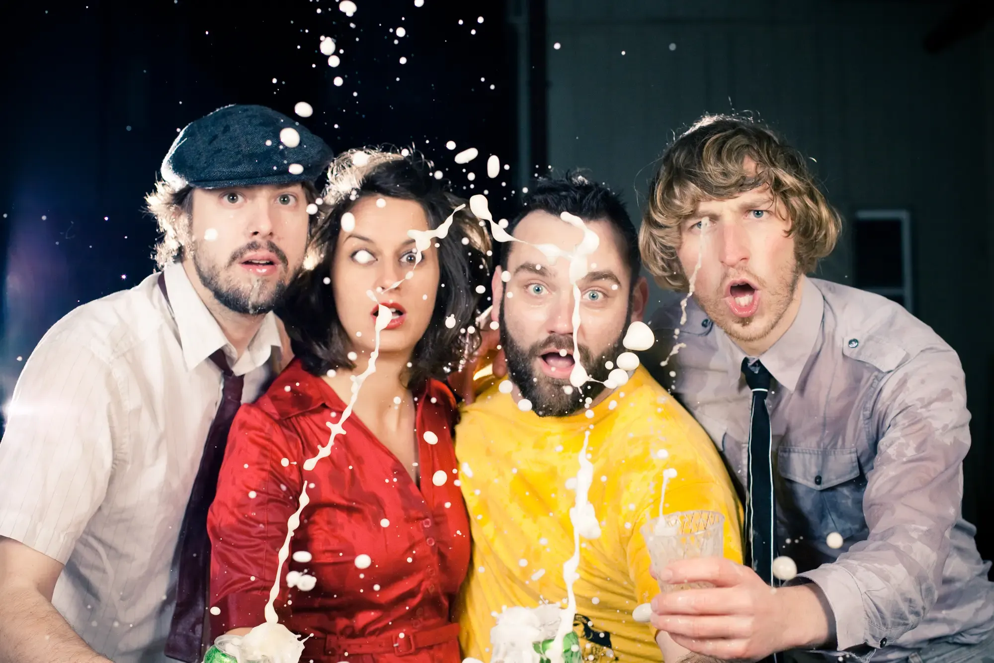 Four people surprised by splashing foam from a drink, wearing a red dress, yellow shirt, gray shirt, and hat.