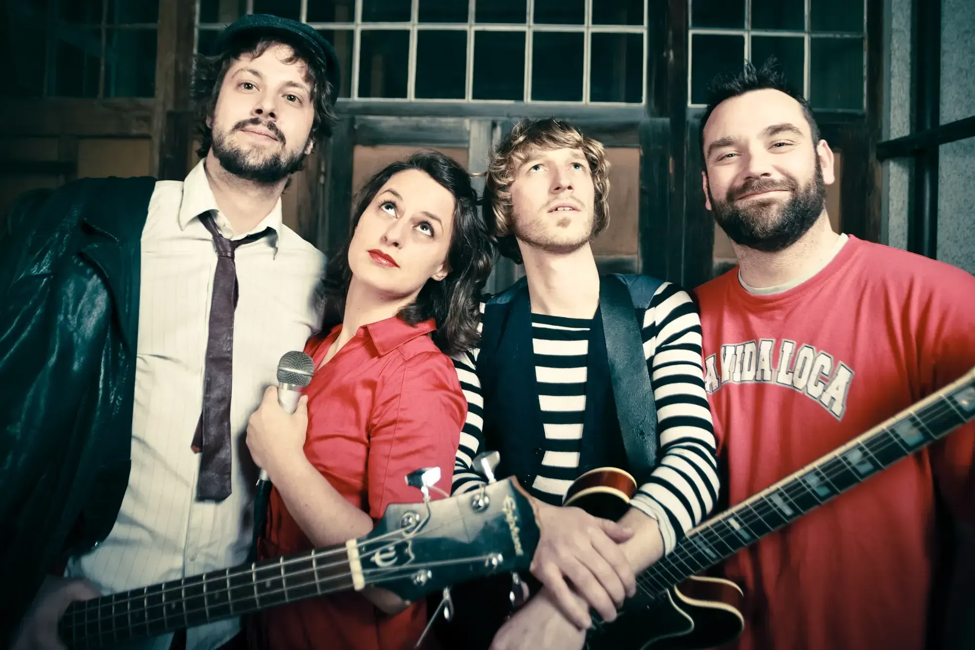 Band portrait of the Budget Boozers posing together in front of an old wooden door, one holding a bass guitar.