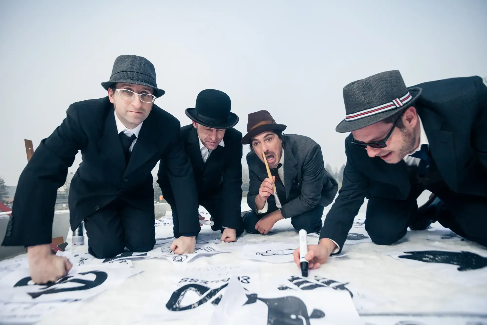 The Büro Destruct team kneeling and drawing directly onto large sheets of paper spread across a rooftop.