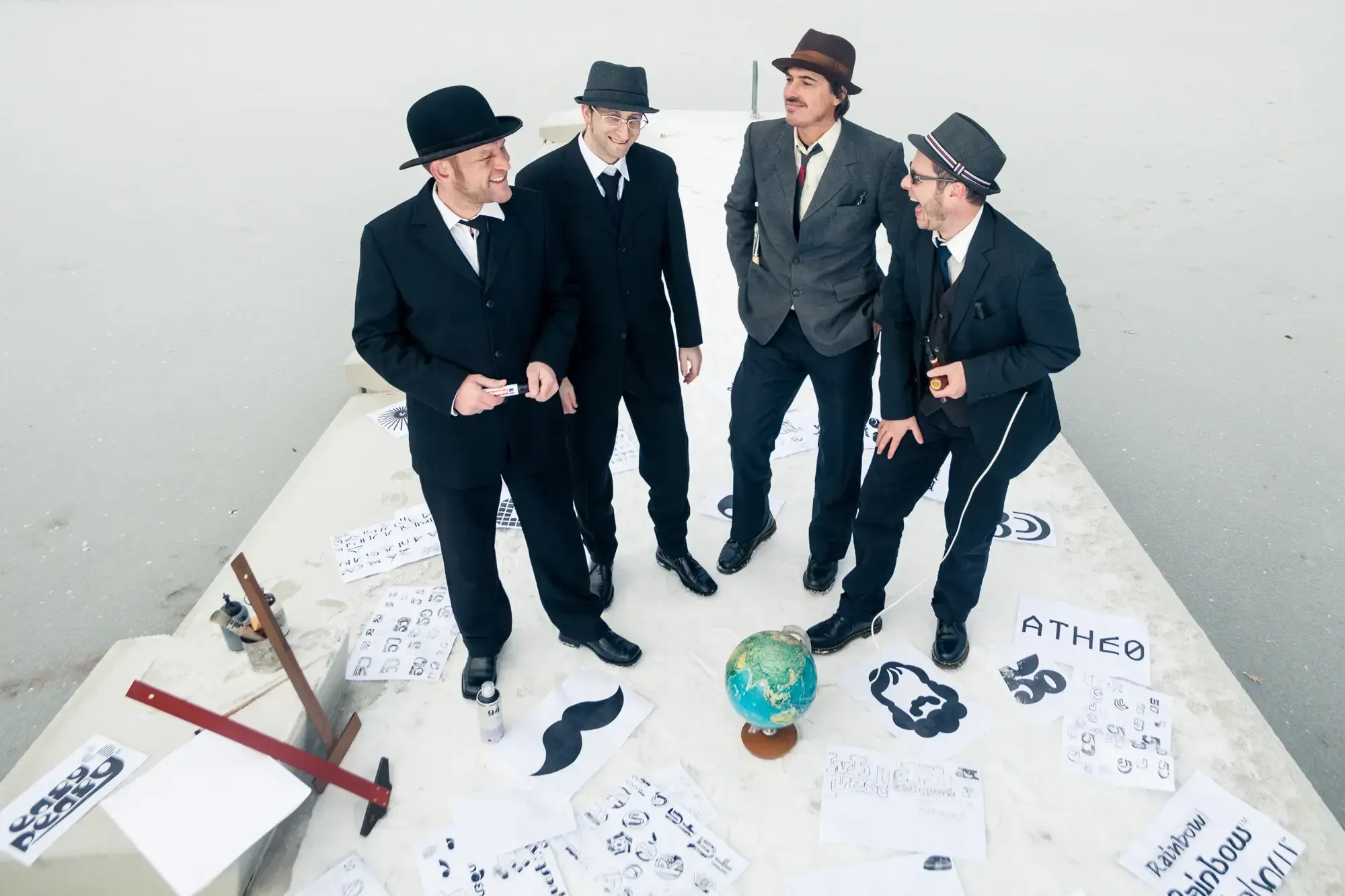 The Büro Destruct team standing and laughing around a globe and scattered logo sketches on a rooftop.
