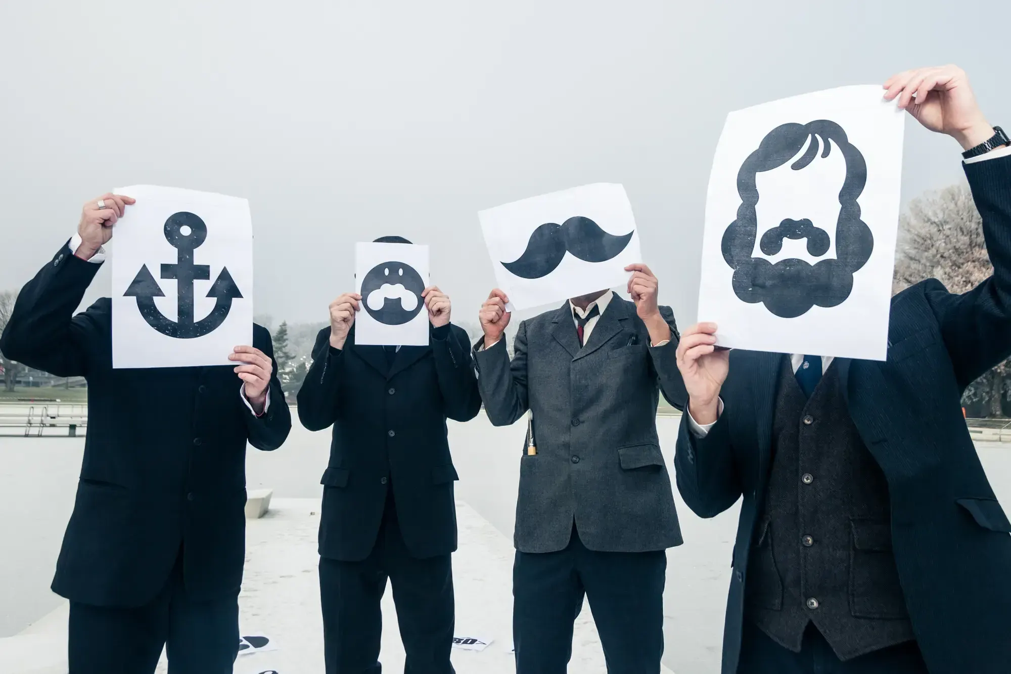 The Büro Destruct team holding up printed paper cutouts of their anchor, beard, moustache and hair logos in front of their faces.