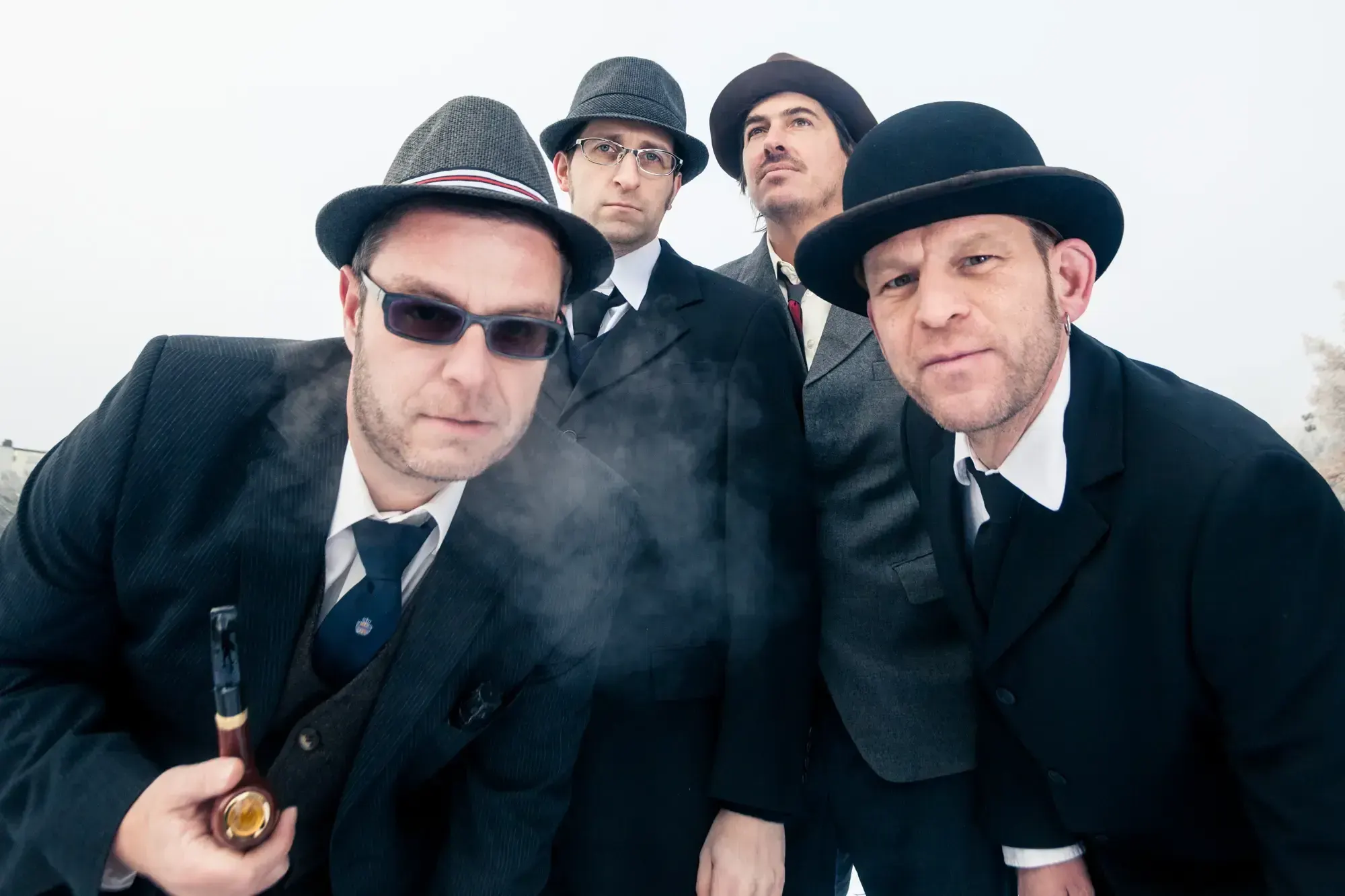 The Büro Destruct design team in suits and hats posing closely together, one smoking a pipe.