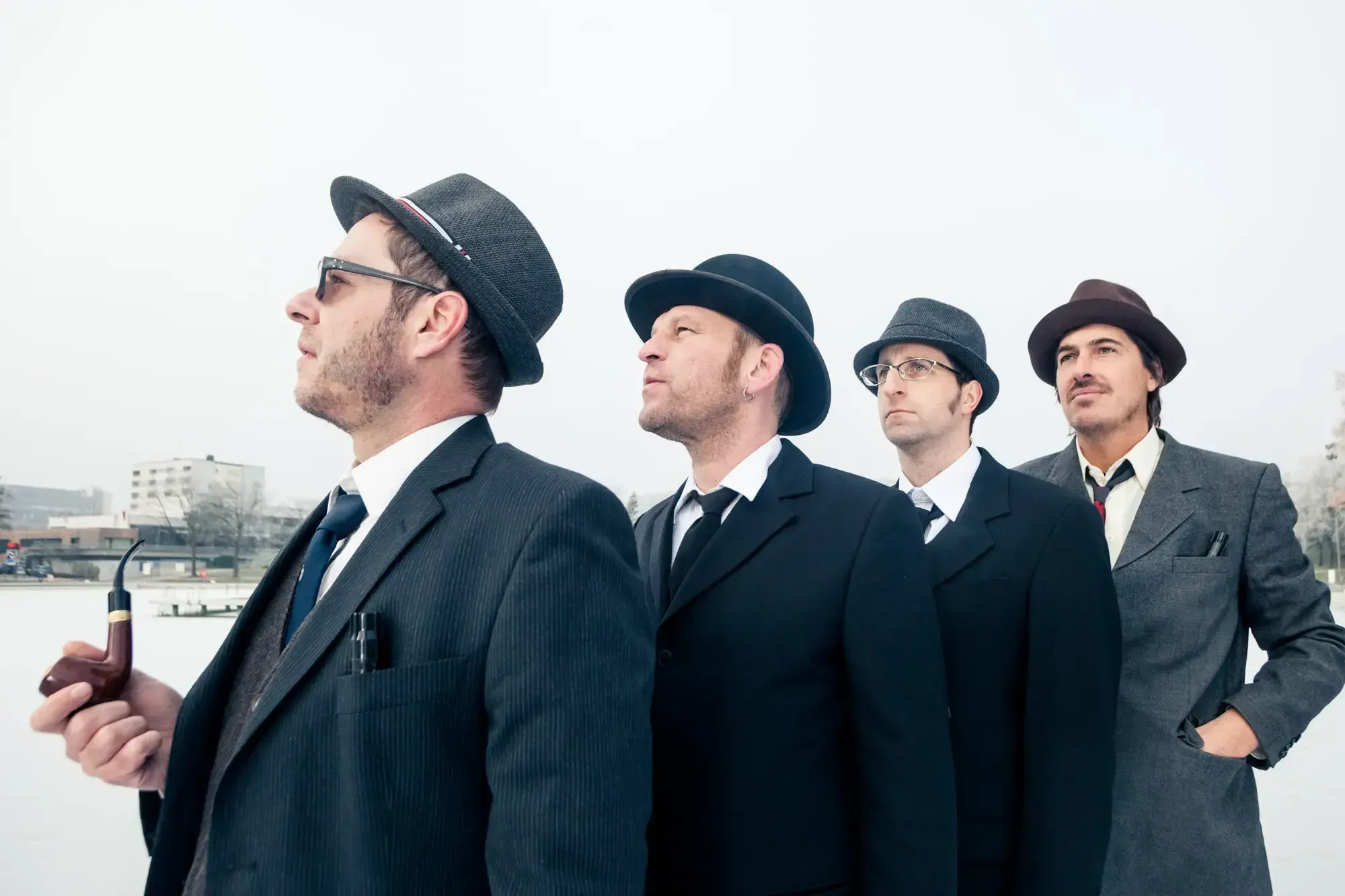 The Büro Destruct design team in suits and hats posing in profile against an overcast sky.