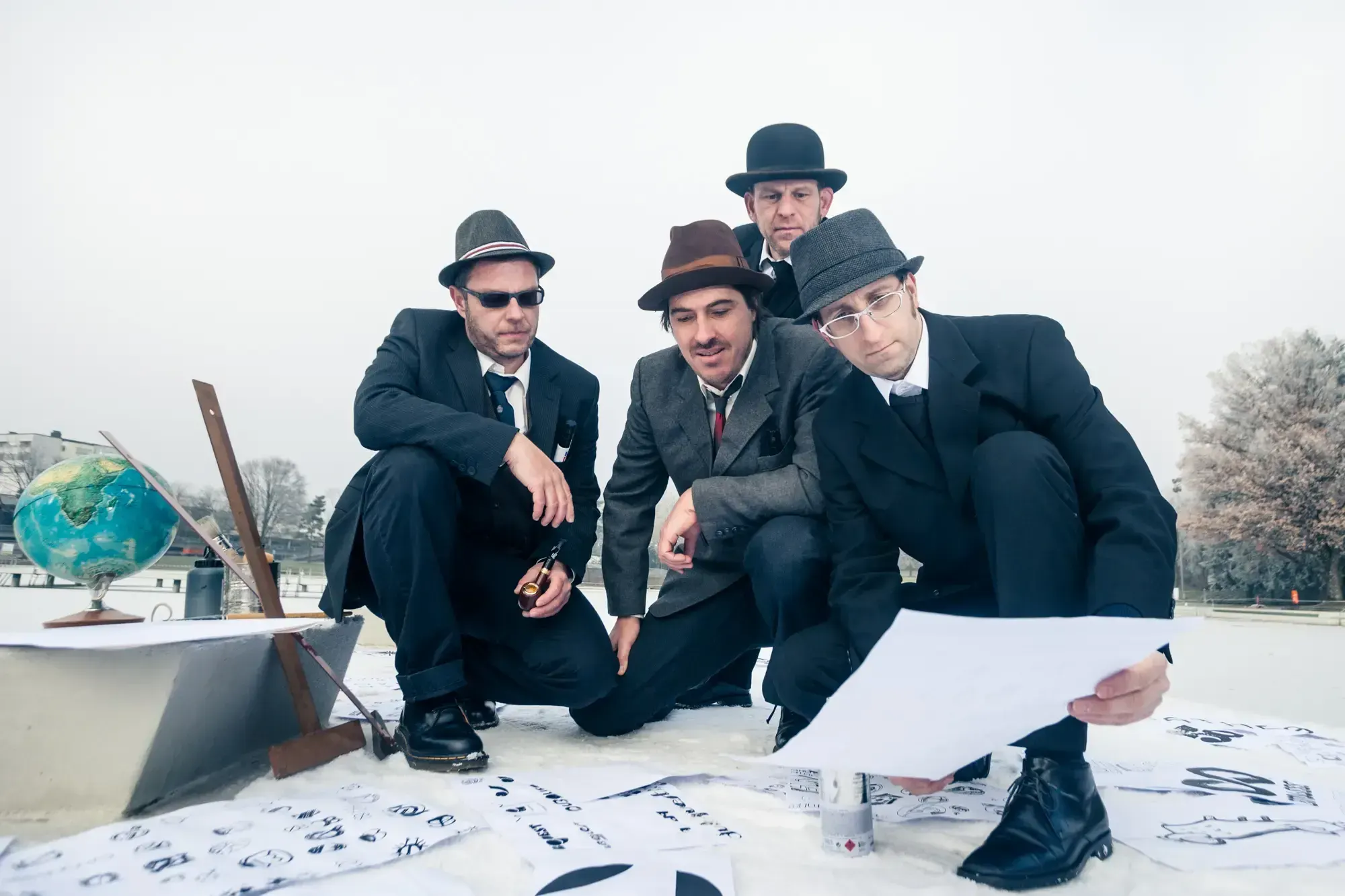 The Büro Destruct design team in suits and hats kneeling around logo sketches on a rooftop.