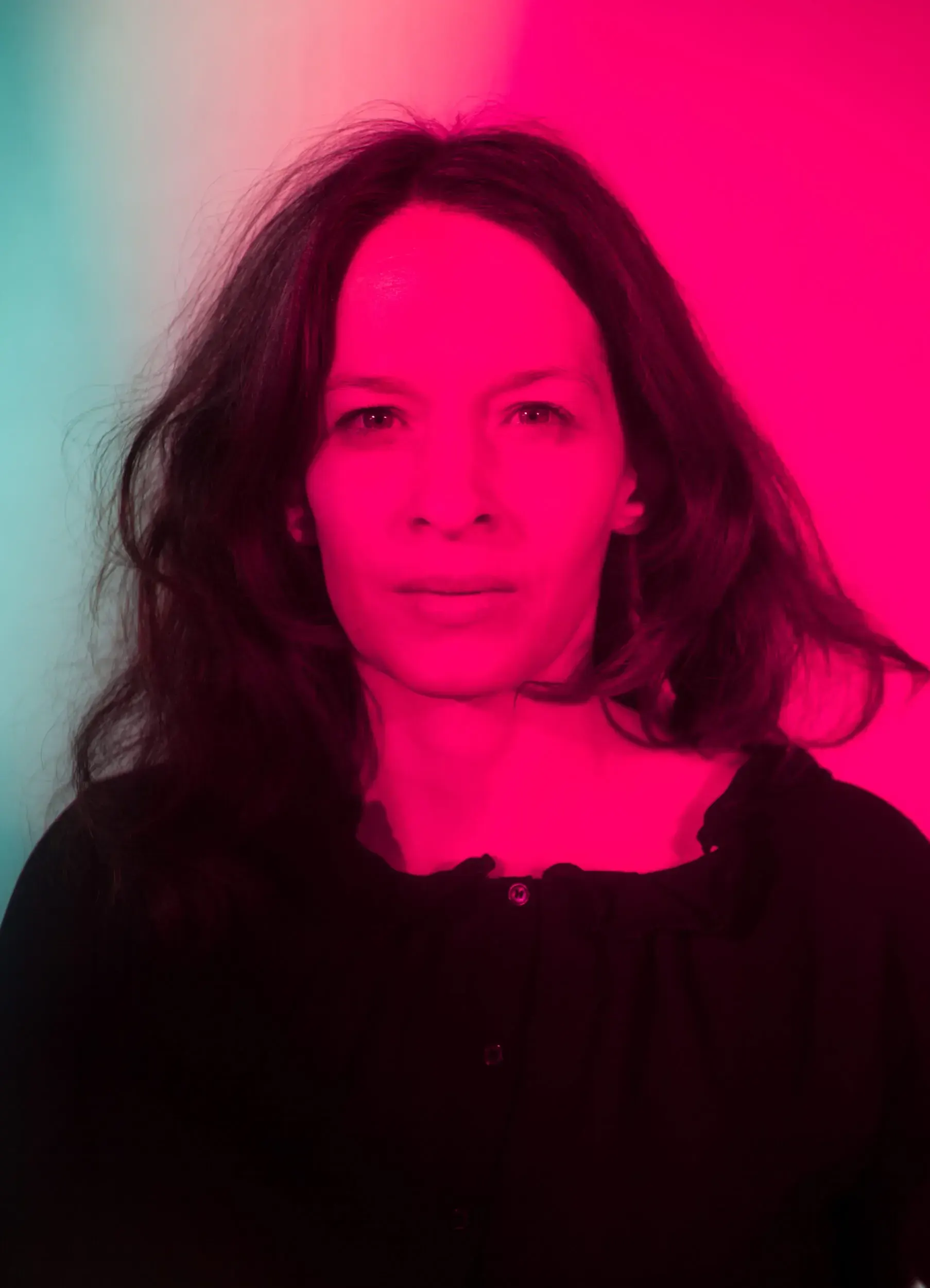 Portrait of actress Carolin Conrad lit by pink and teal gel light against a plain background.