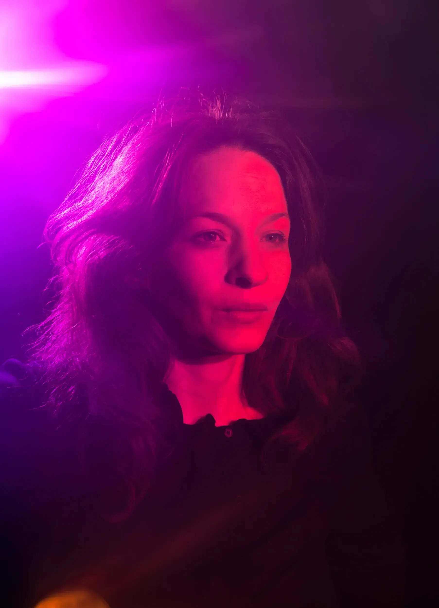 Portrait of actress Carolin Conrad lit by purple stage light, looking to the side.