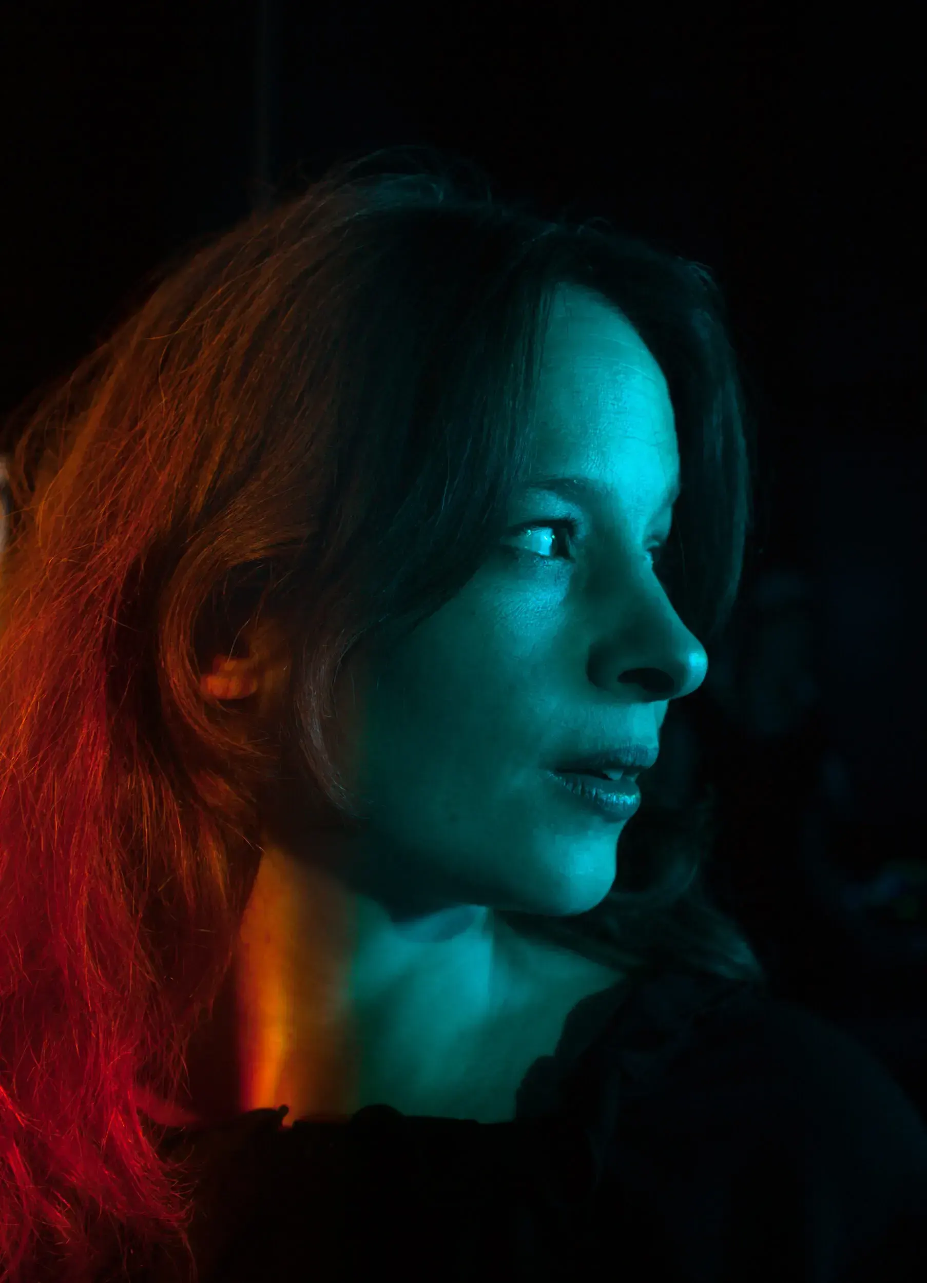 Profile portrait of actress Carolin Conrad lit in red and teal against a dark background.