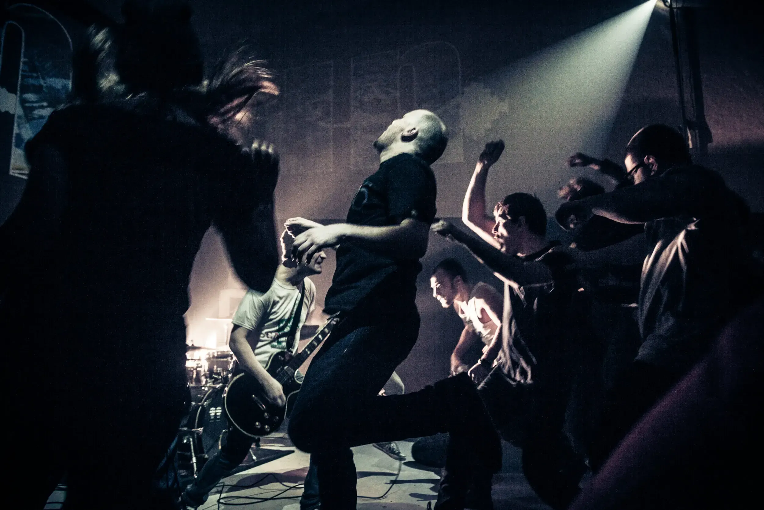 Band performing energetically on stage while the crowd raises their hands and jumps along.