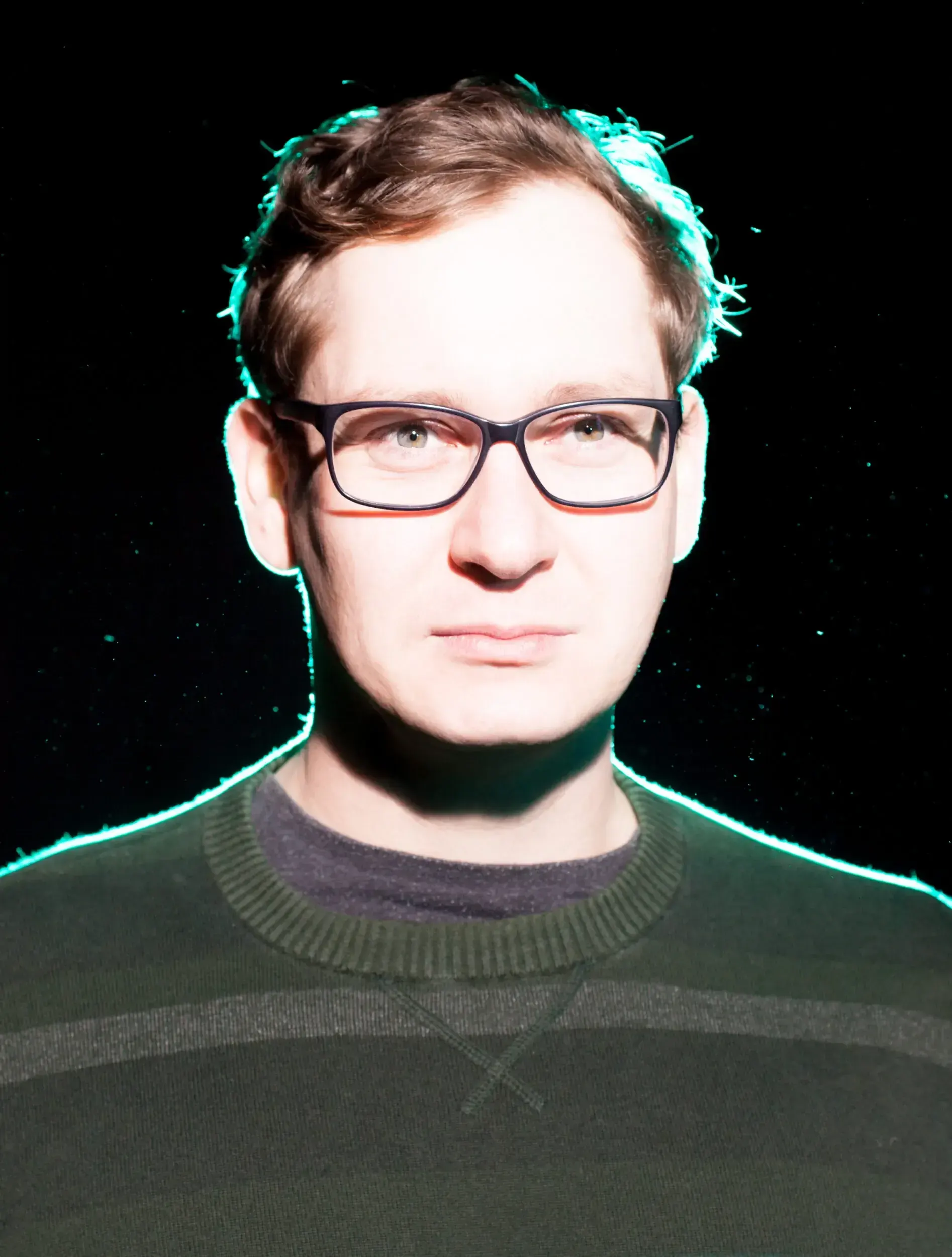 Portrait of Christian Baumbach wearing glasses, lit with a glowing teal outline against a black background.
