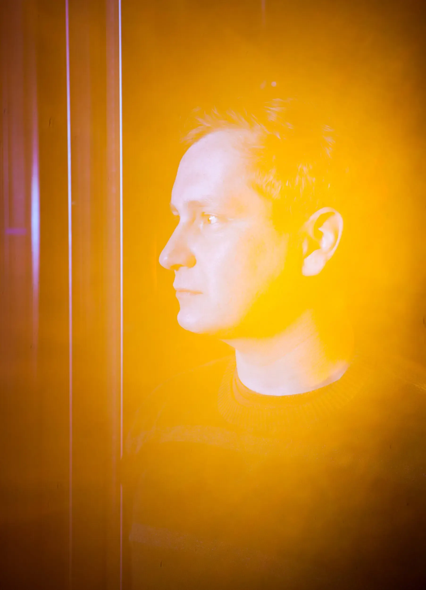 Profile portrait of Christian Baumbach bathed in warm orange light.