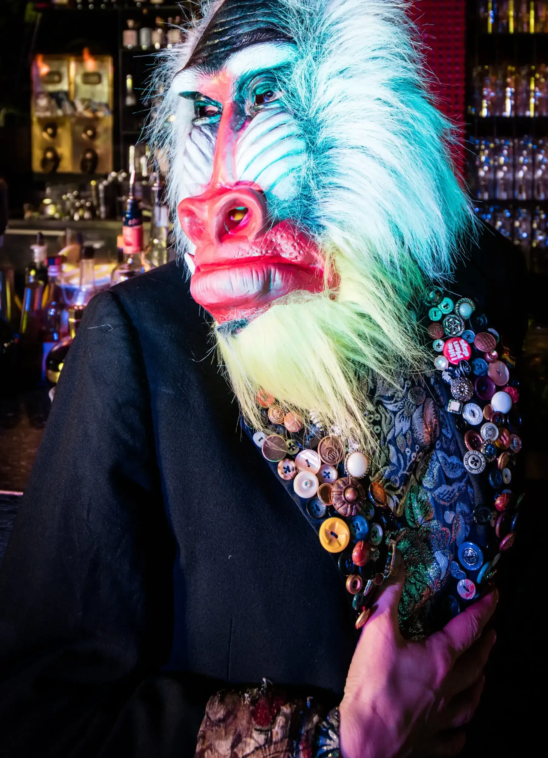 Close-up of a guest in a baboon mask wearing a jacket covered in decorative buttons.