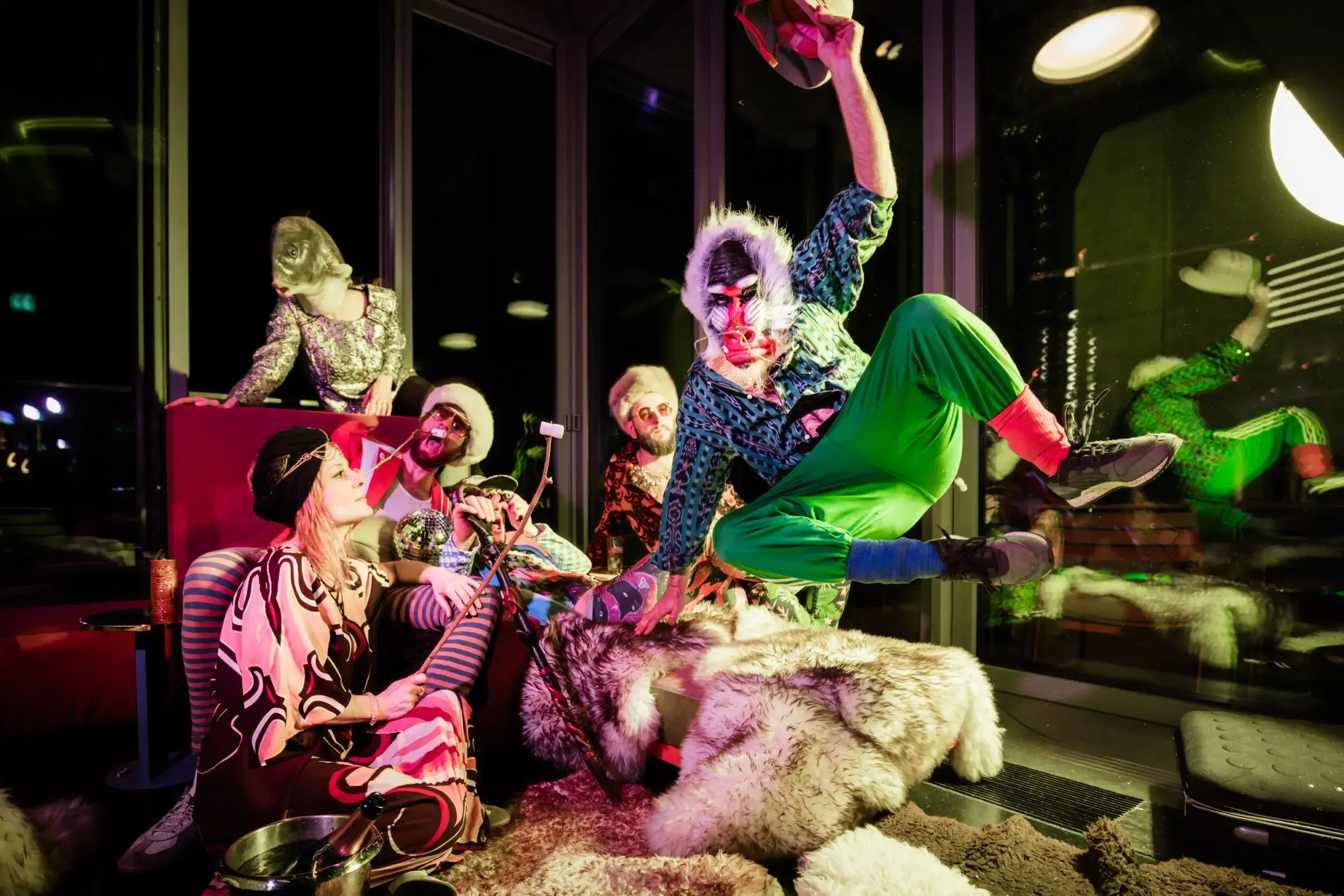 Guest in a baboon mask jumping energetically over a group seated on fur throws.
