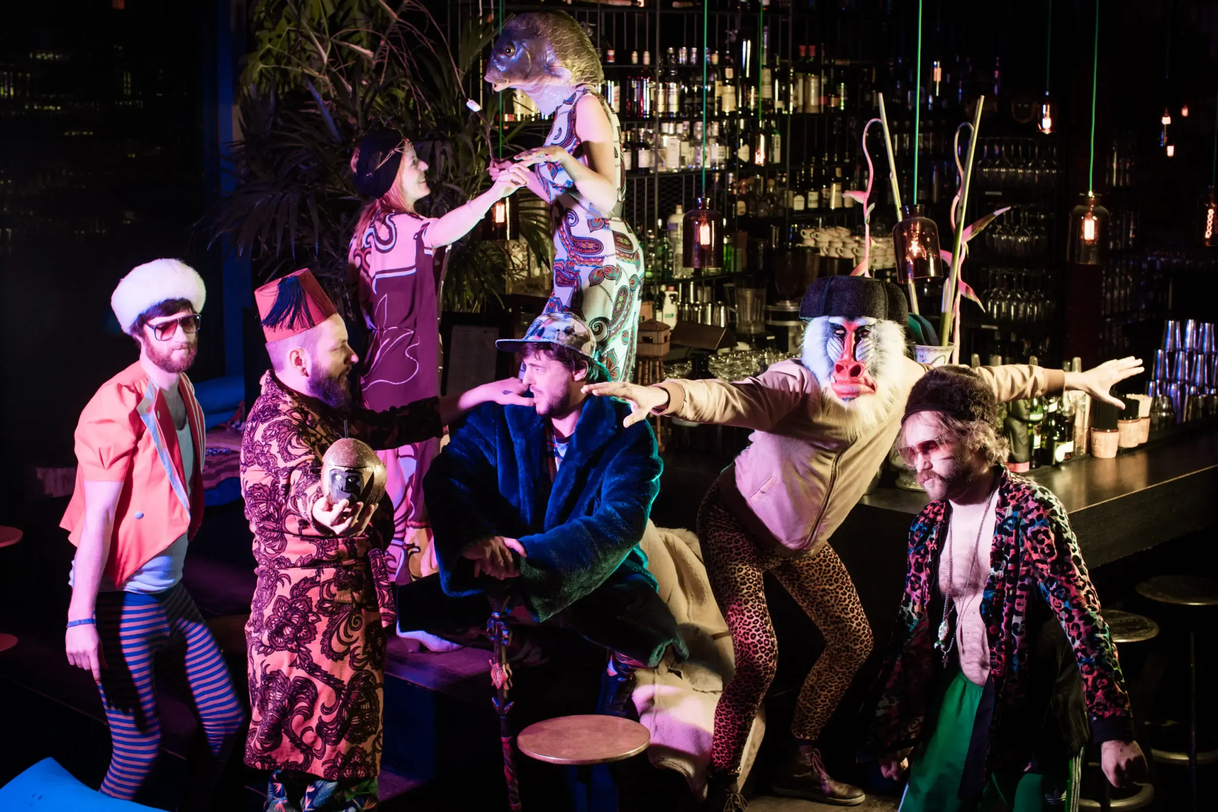 Costumed guests dancing playfully together at a bar strung with lights.