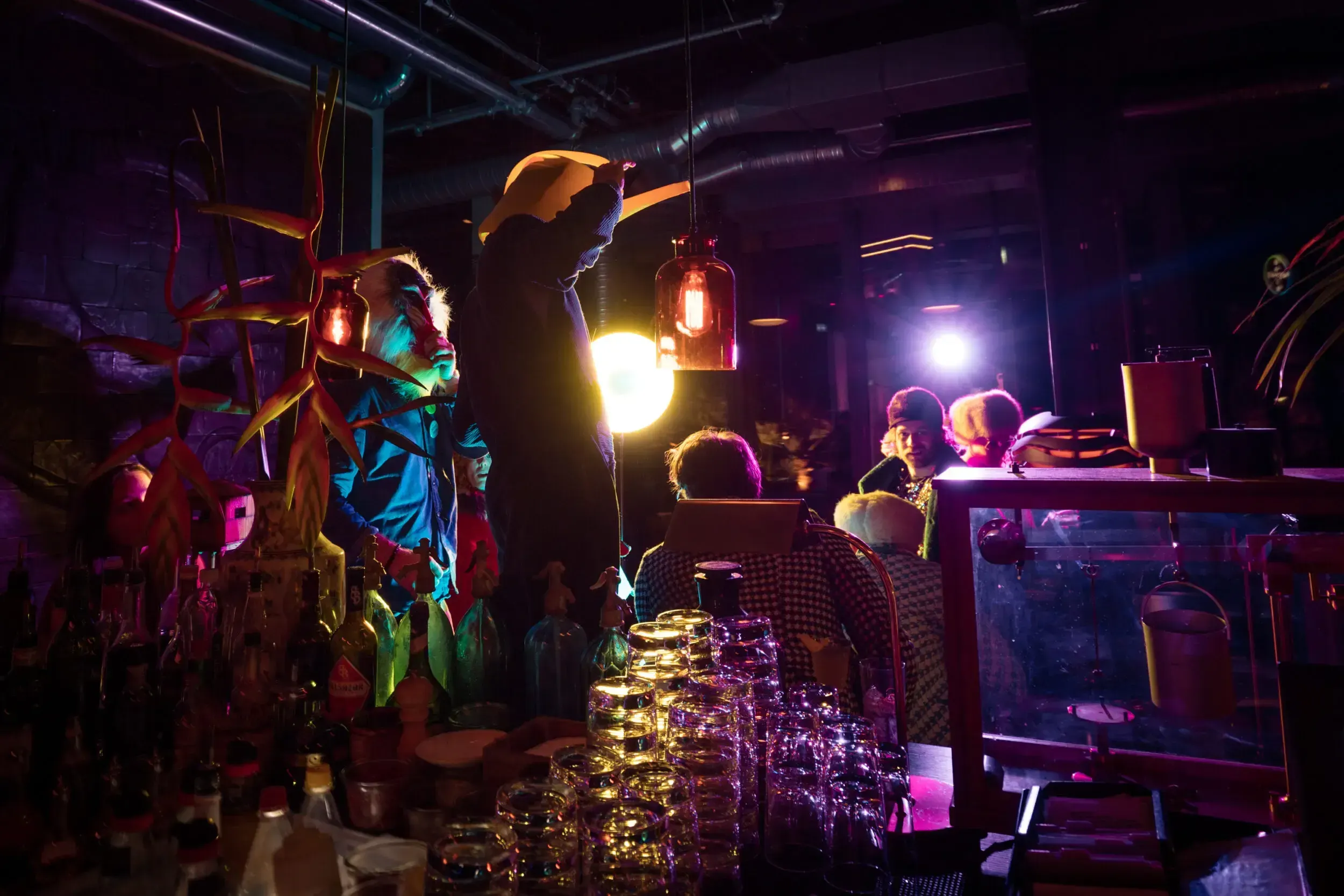 Costumed guests seated at a bar decorated with hanging lanterns and glassware.
