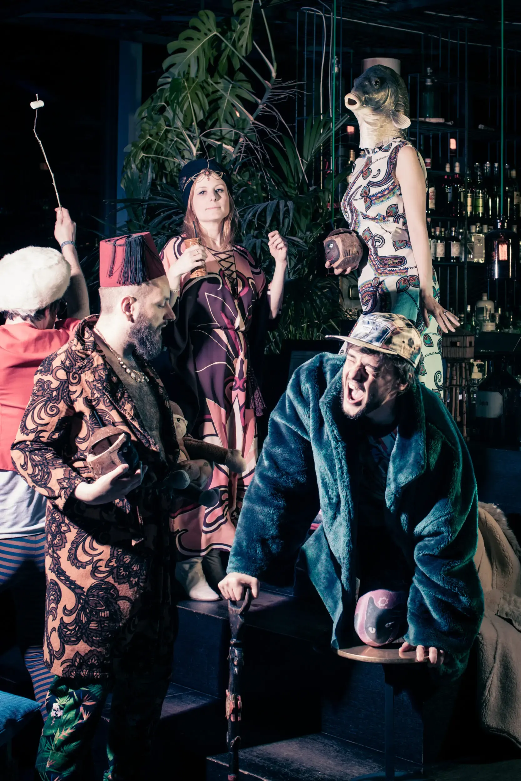 Costumed guests posed dramatically on bar furniture, one leaning on a cane.