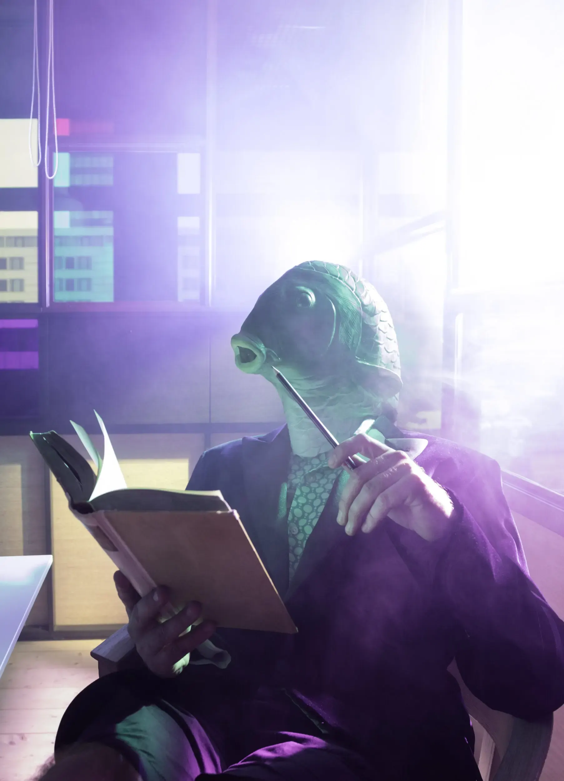 Guest in a green bird mask reading a book in an office lit in green and purple.