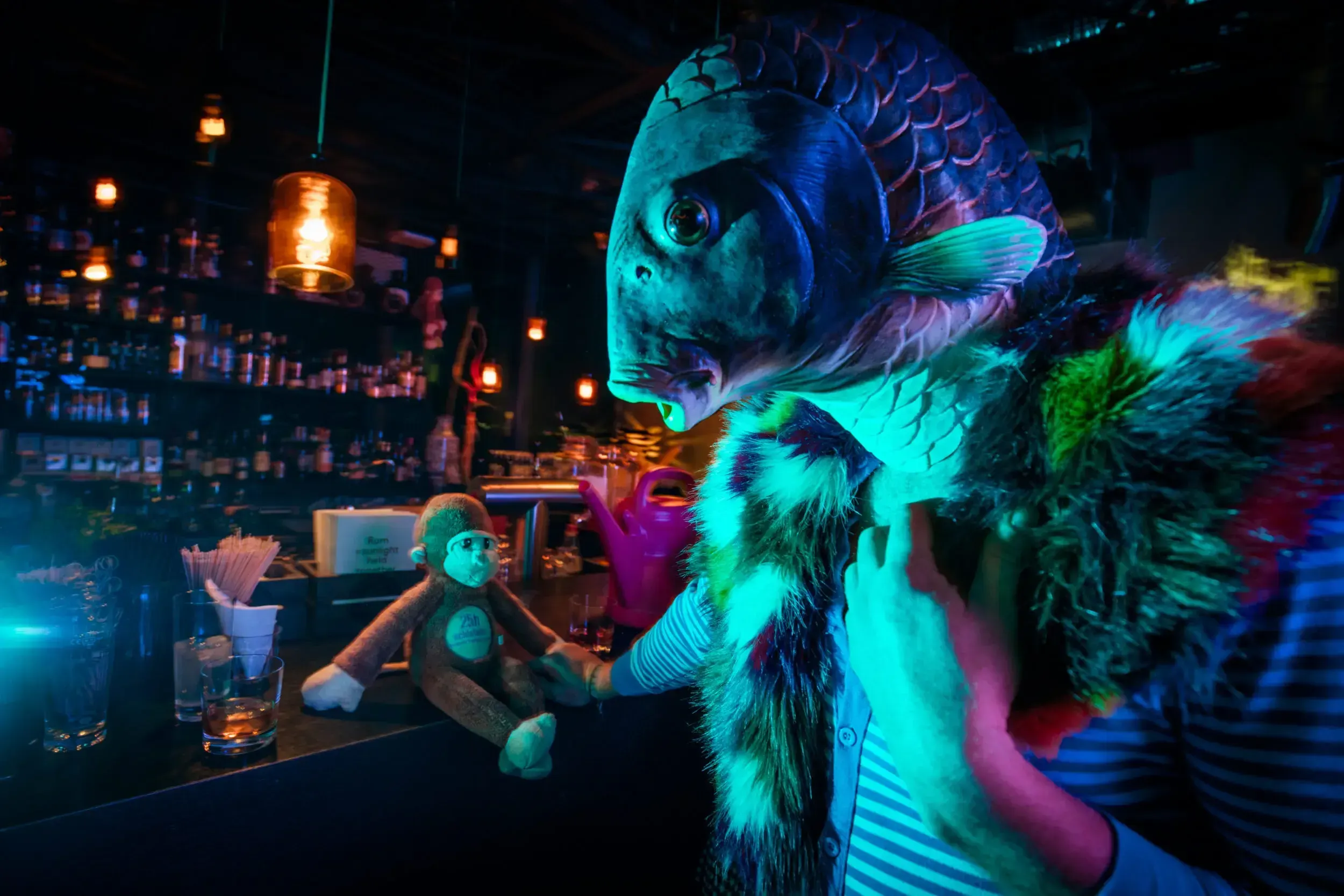 Guest in a fish mask at the bar beside a toy monkey and a pink watering can.
