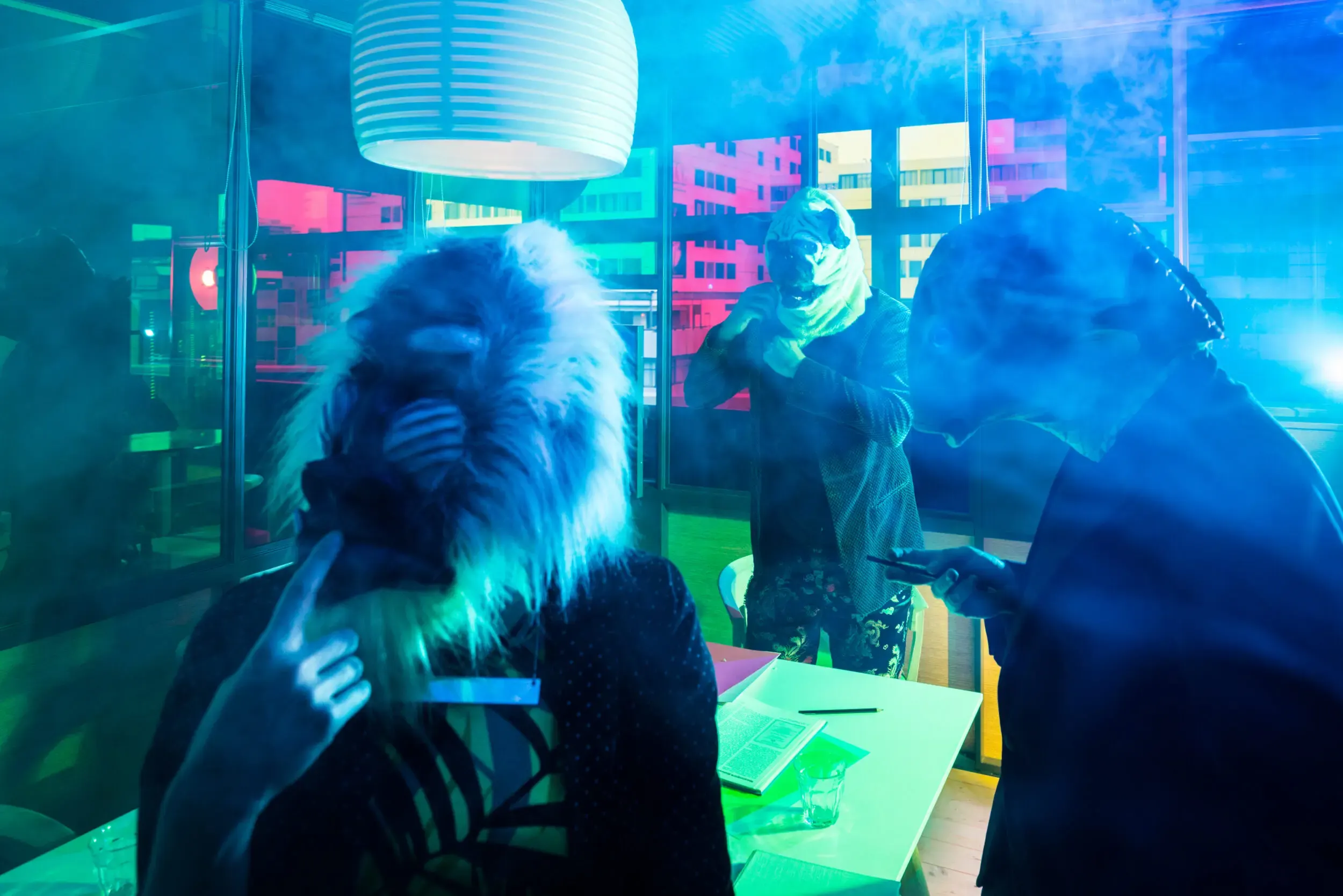 Guests in gorilla masks standing in an office lit in blue.