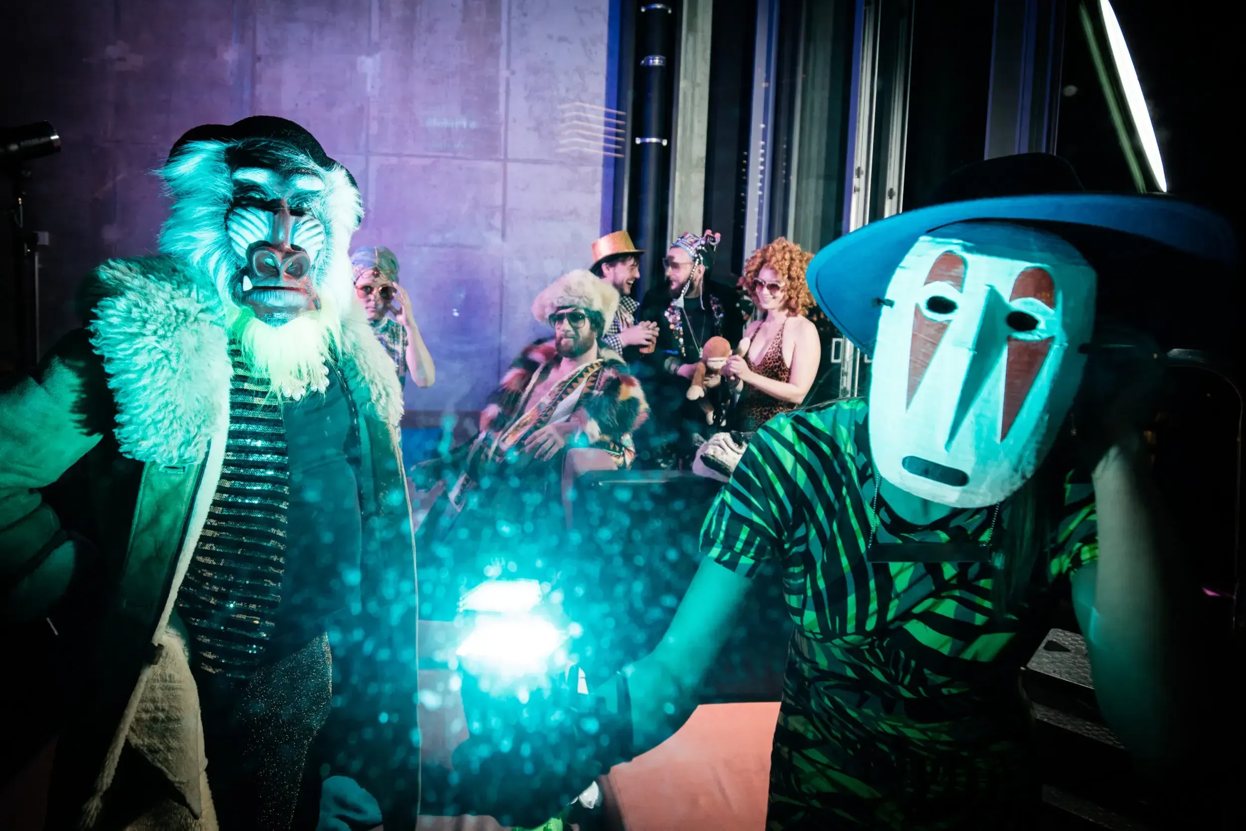 Guests in a baboon mask and a carved wooden mask lit in blue light at the party.